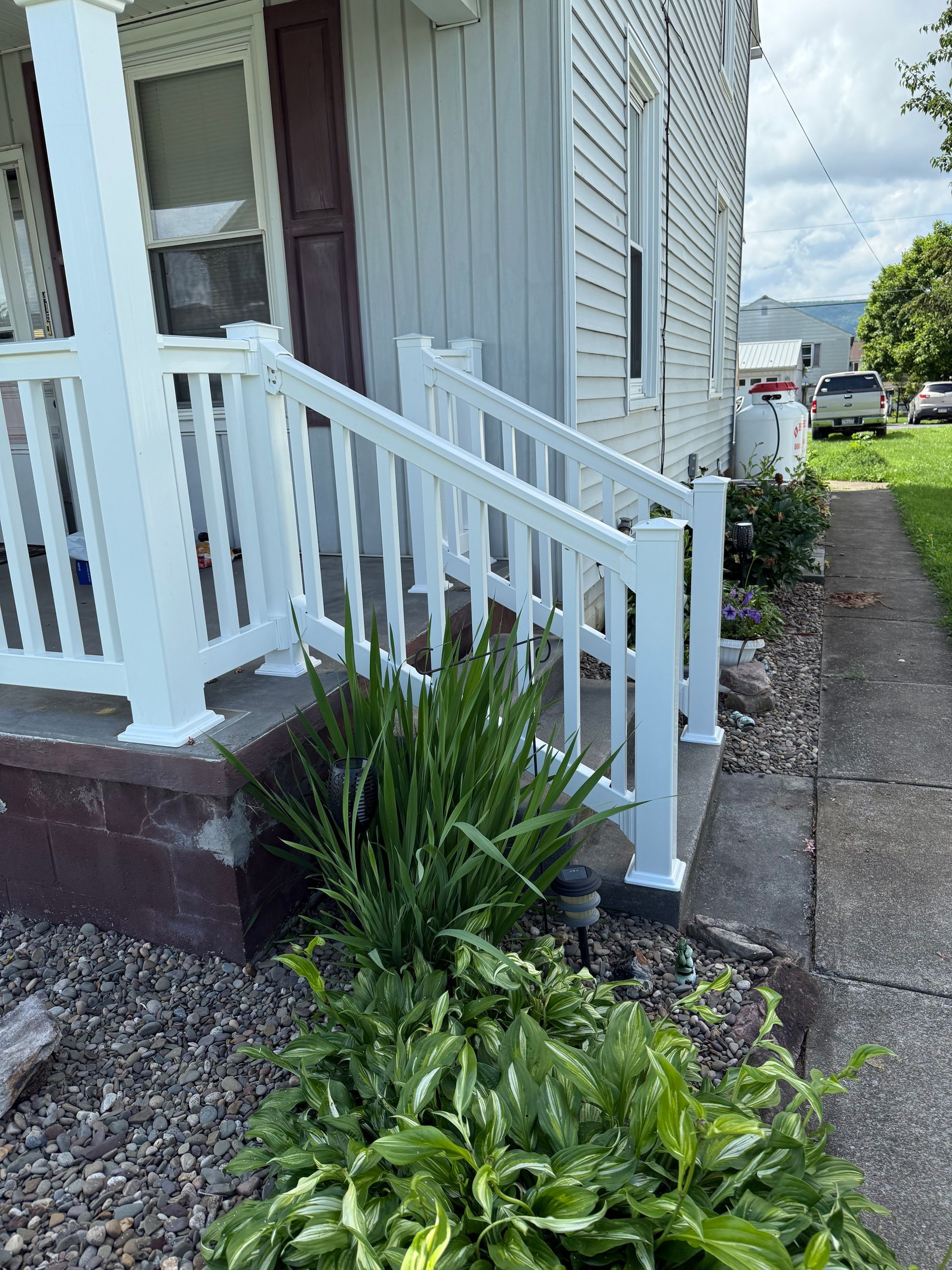White porch railing and steps leading up to a white house with landscaping.