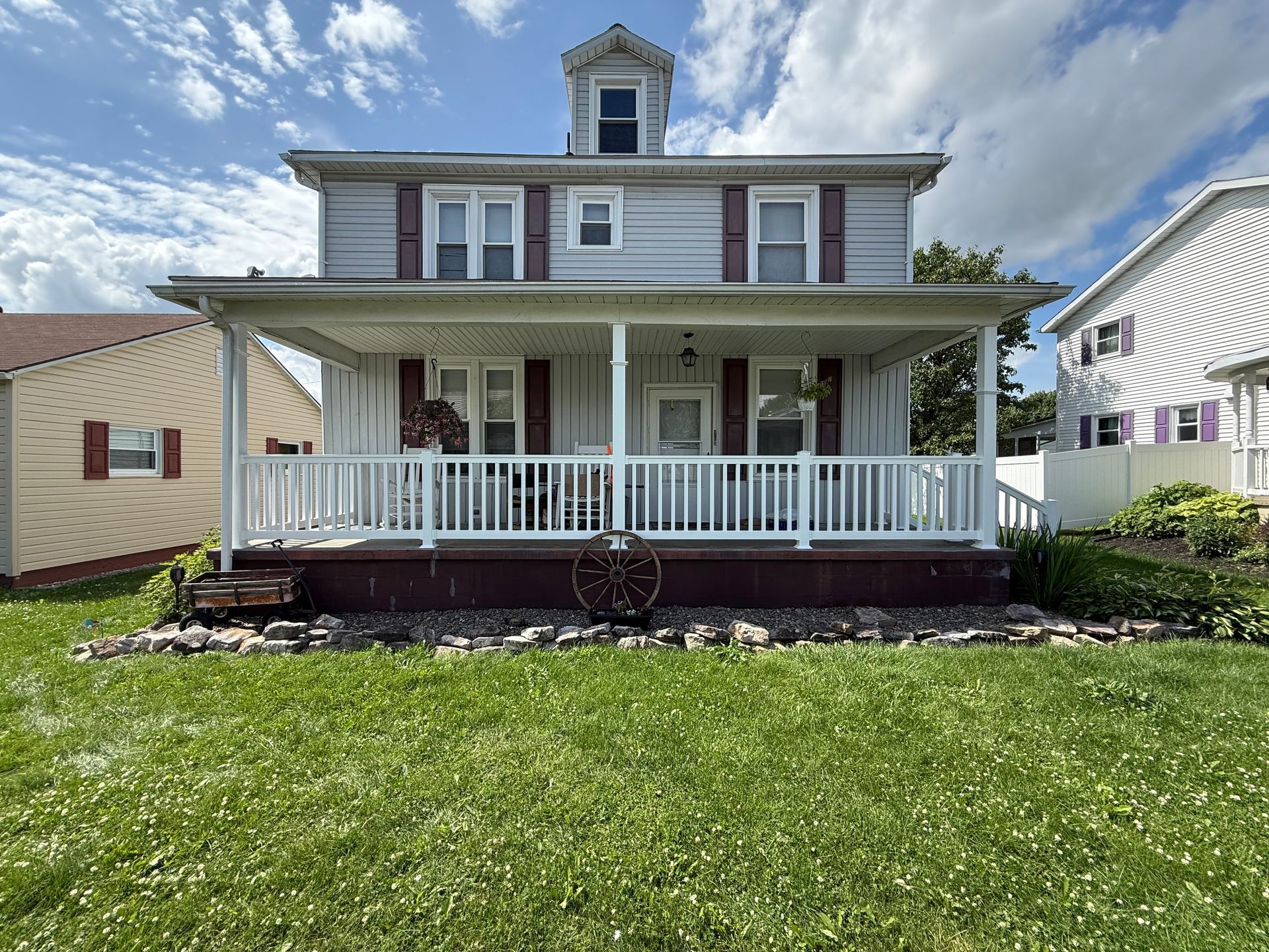 Two-story house with a porch, light siding, red shutters, and a green lawn.