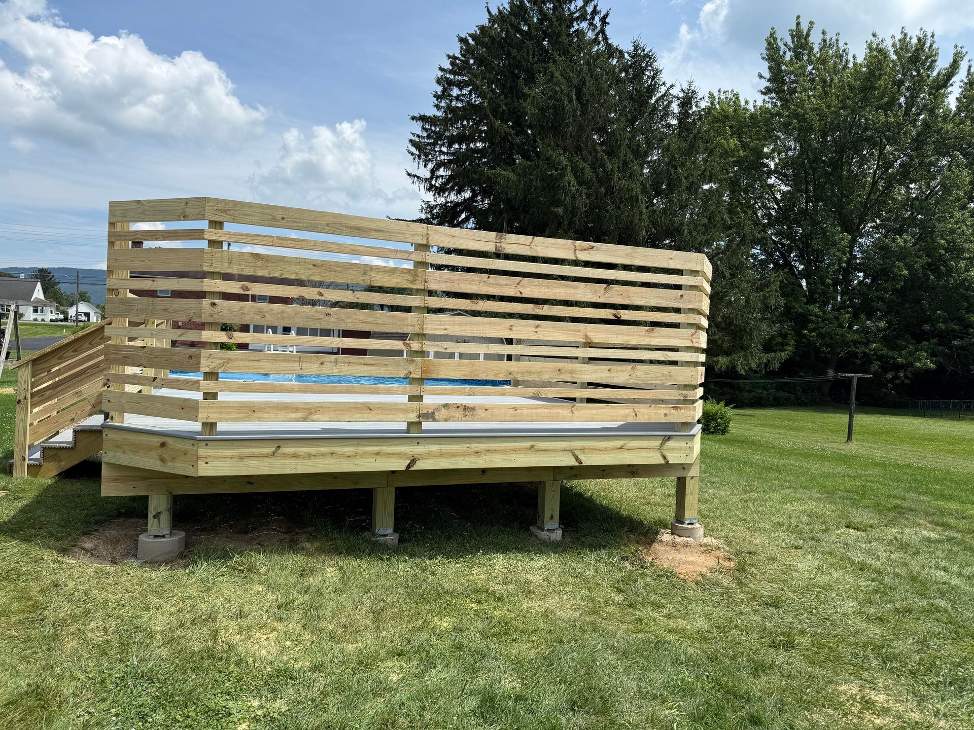 Wooden deck with horizontal railing in a grassy backyard, under a cloudy sky.