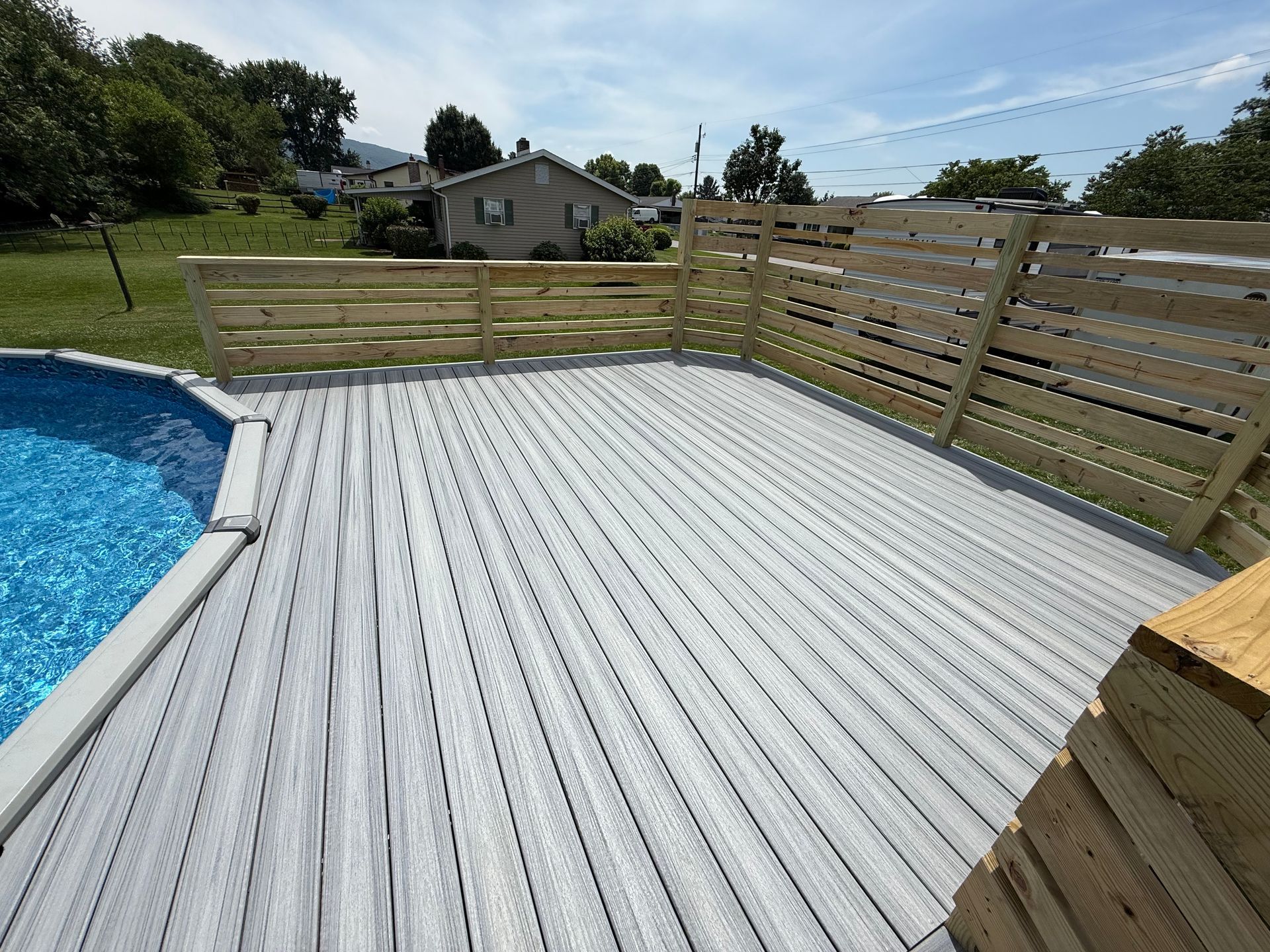 Wooden deck surrounds a blue swimming pool with a horizontal slatted fence.