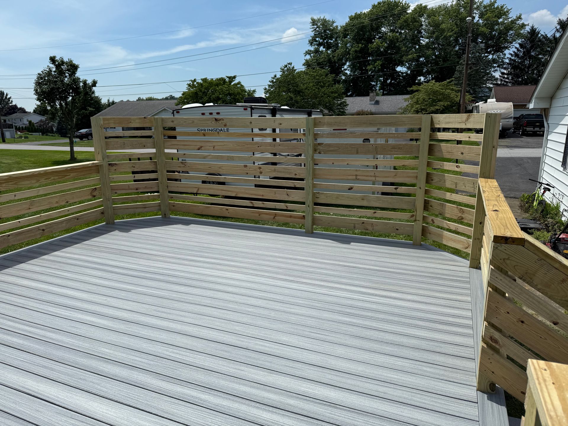 Wooden deck with gray composite flooring and a wooden fence.