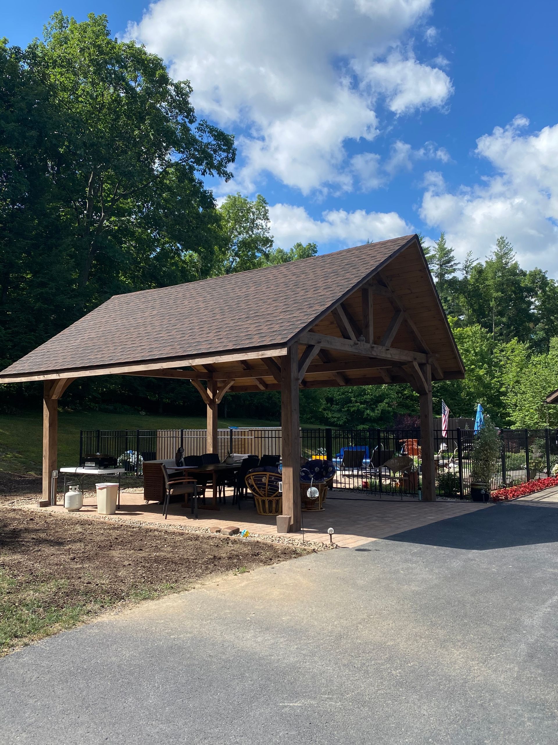 Wooden pavilion with brown roof and picnic tables. Overlooking a playground on a sunny day.