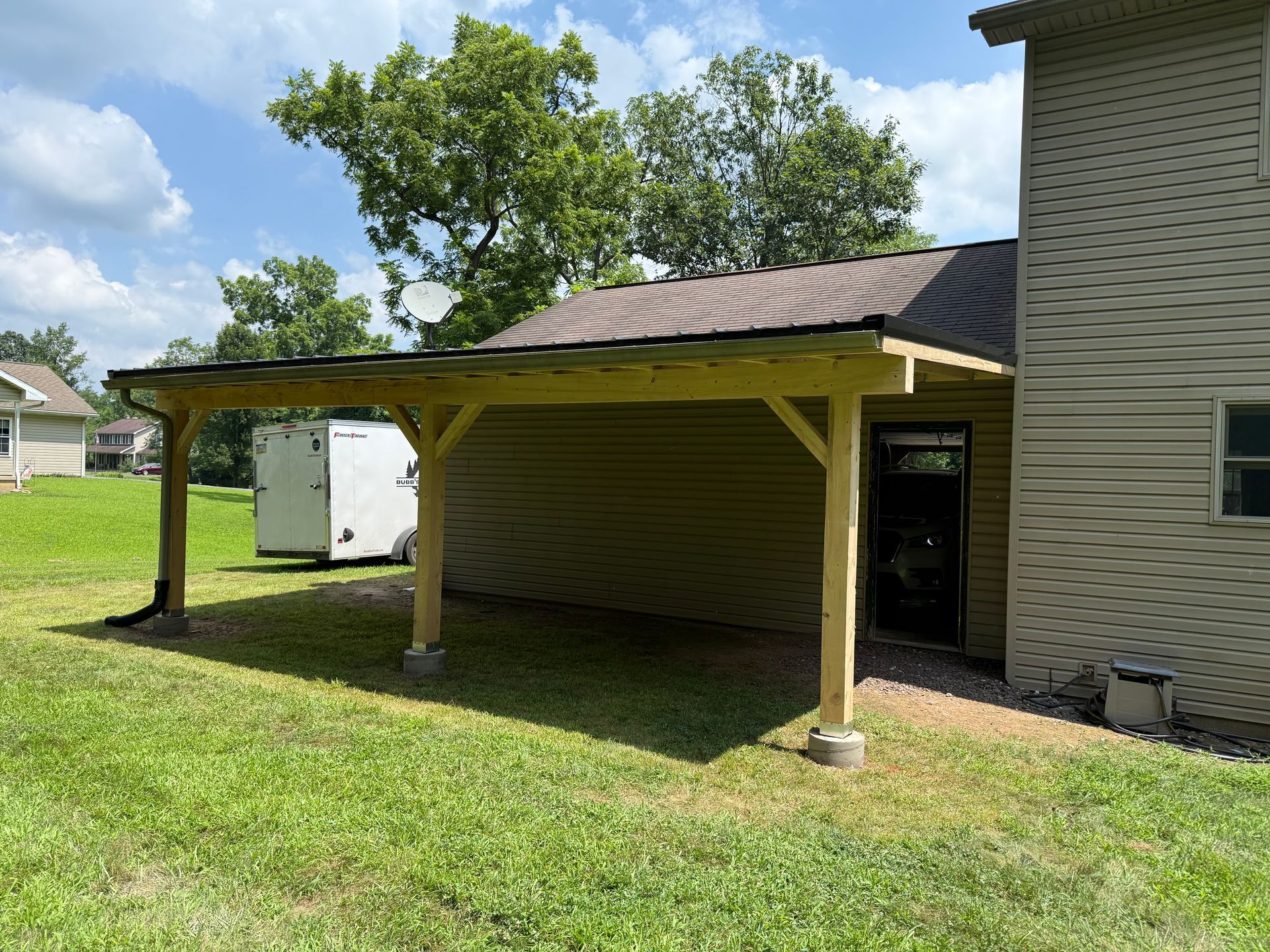 Wooden carport attached to a beige house, with a green lawn.