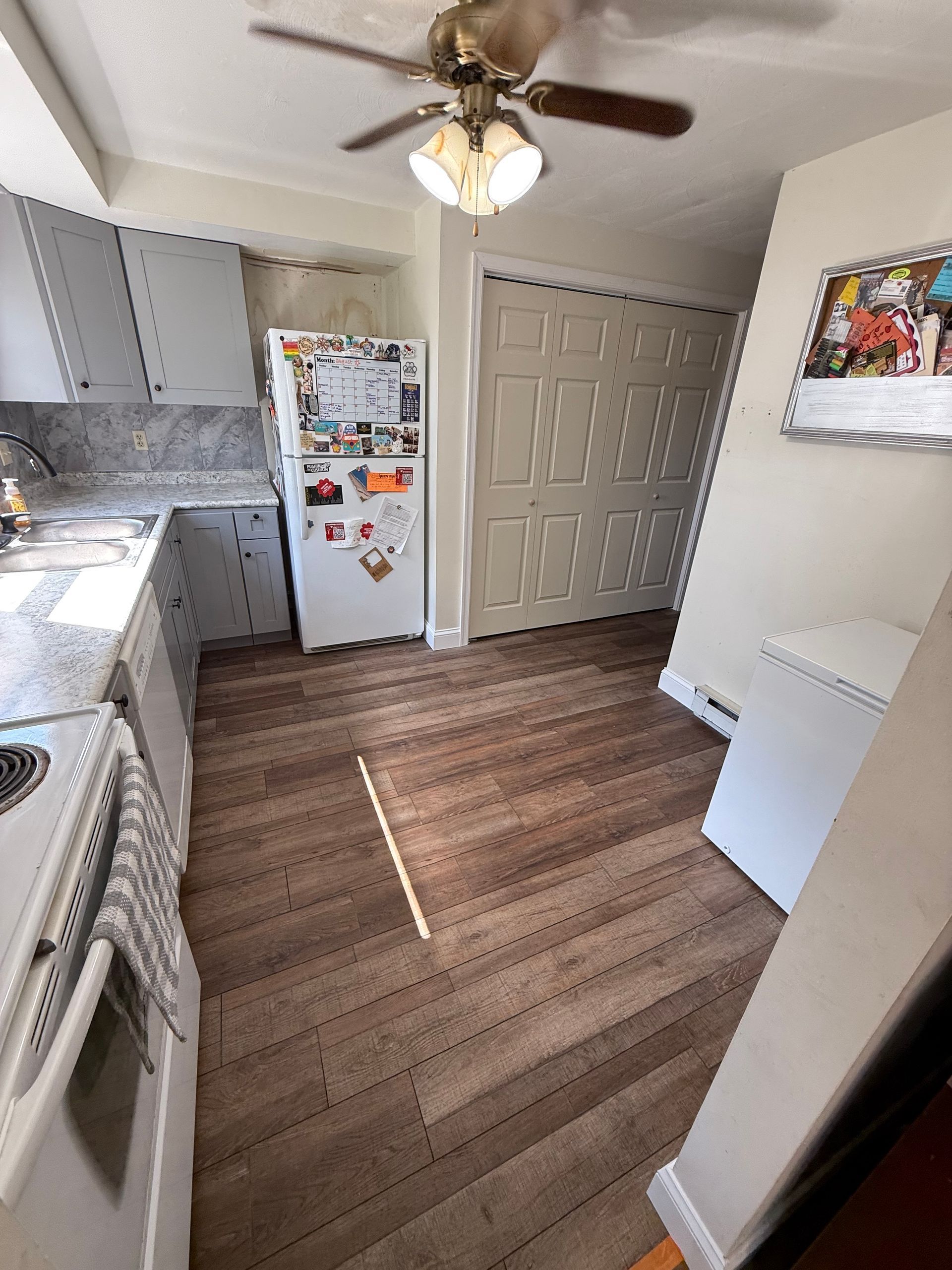 Kitchen with white cabinets, refrigerator, and brown flooring. A ceiling fan is visible.