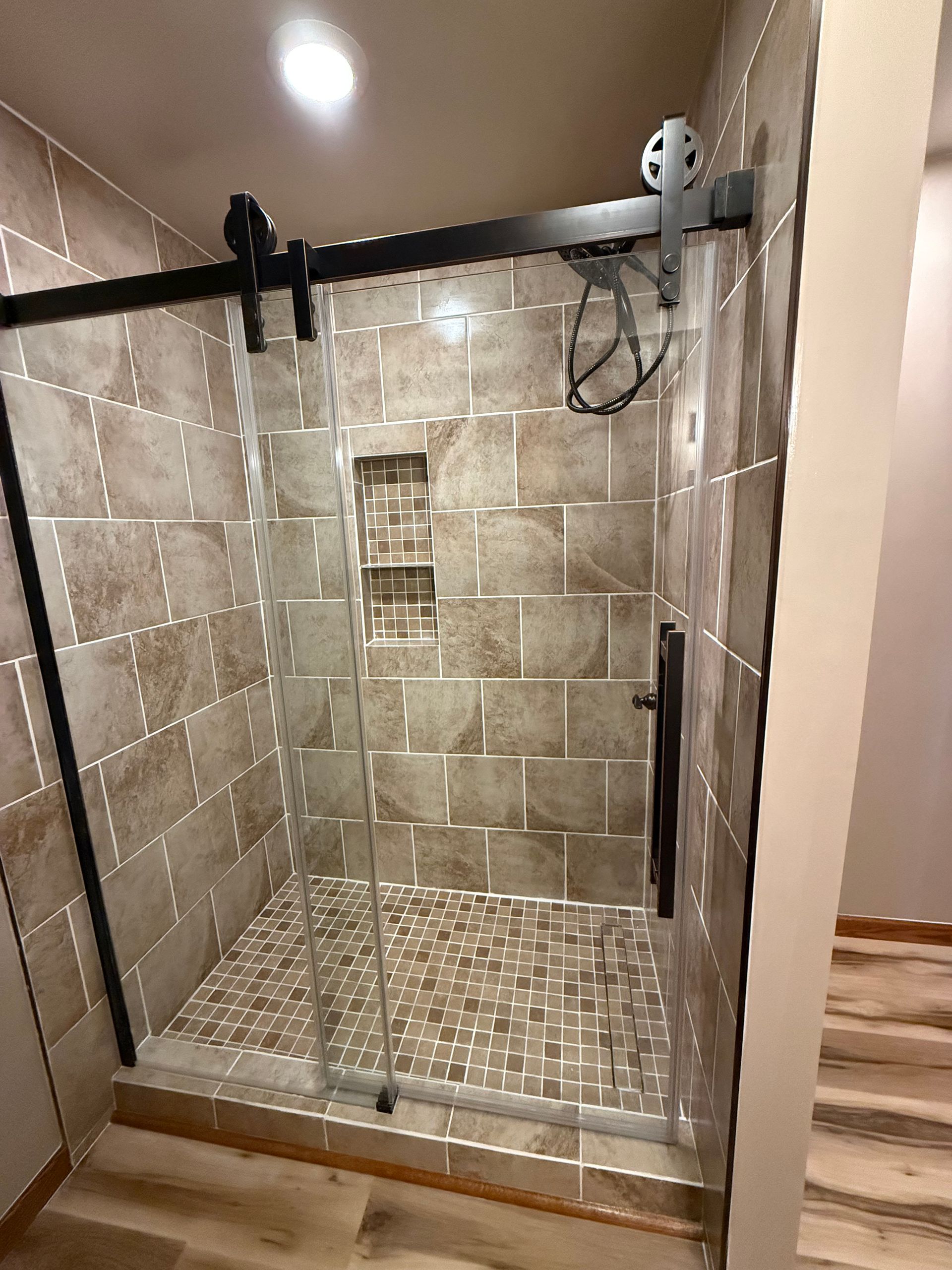 Shower with black framed sliding glass door, pebble floor, and tiled walls.