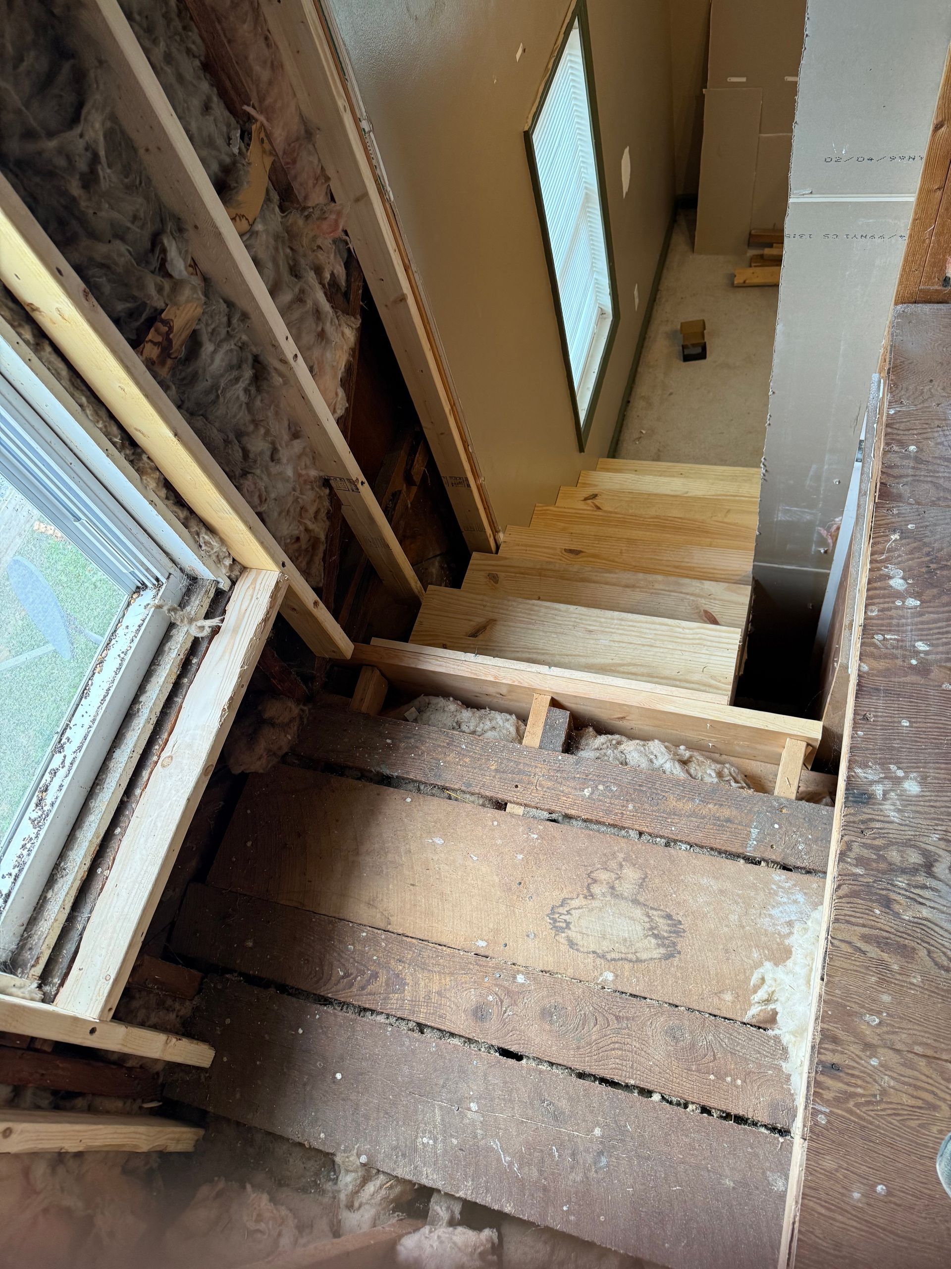 Staircase under construction, exposed wooden steps, insulation, and window frame visible.
