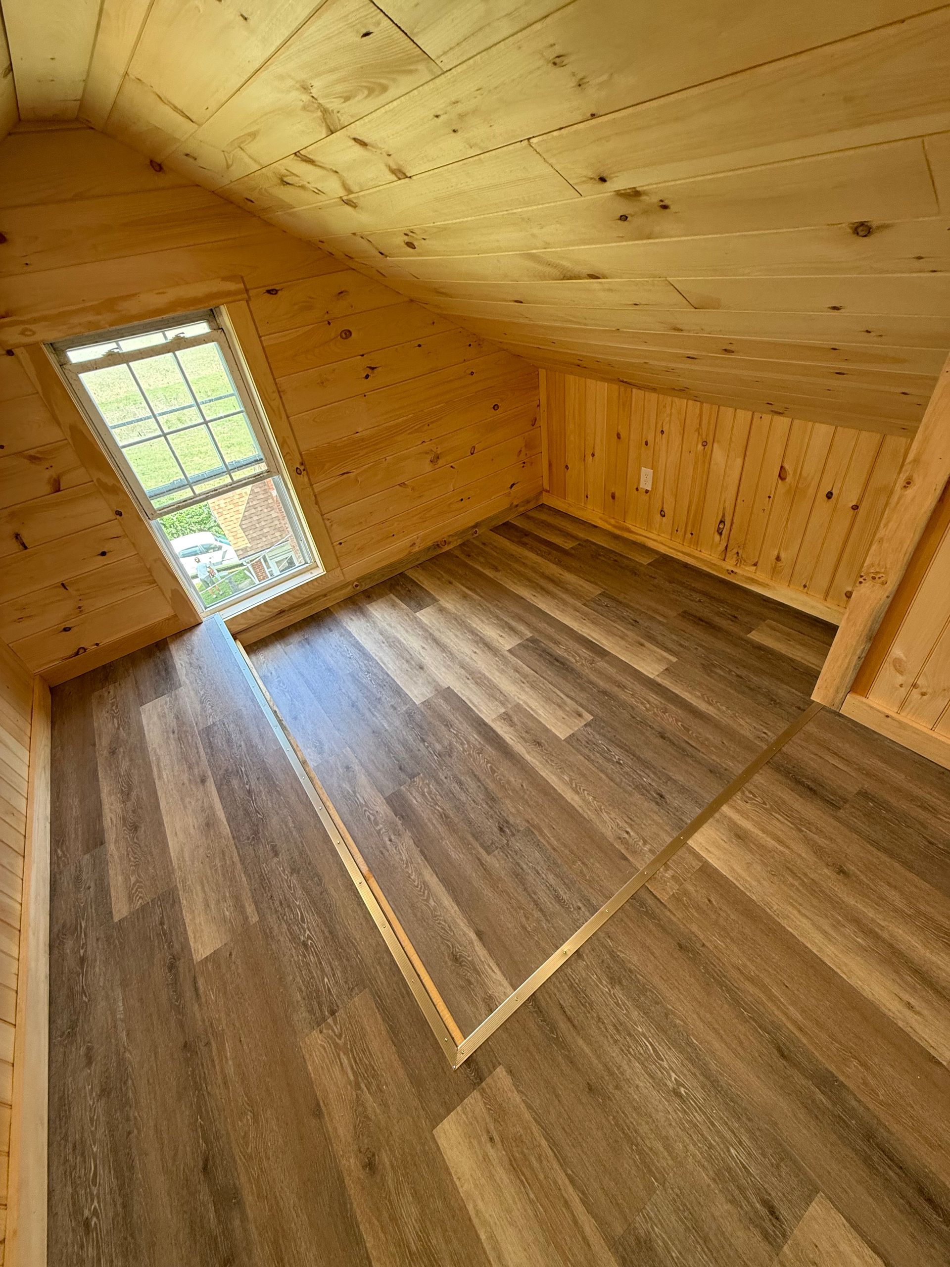 Interior of a small room with wood paneling and flooring, a small window, and a sloped ceiling.
