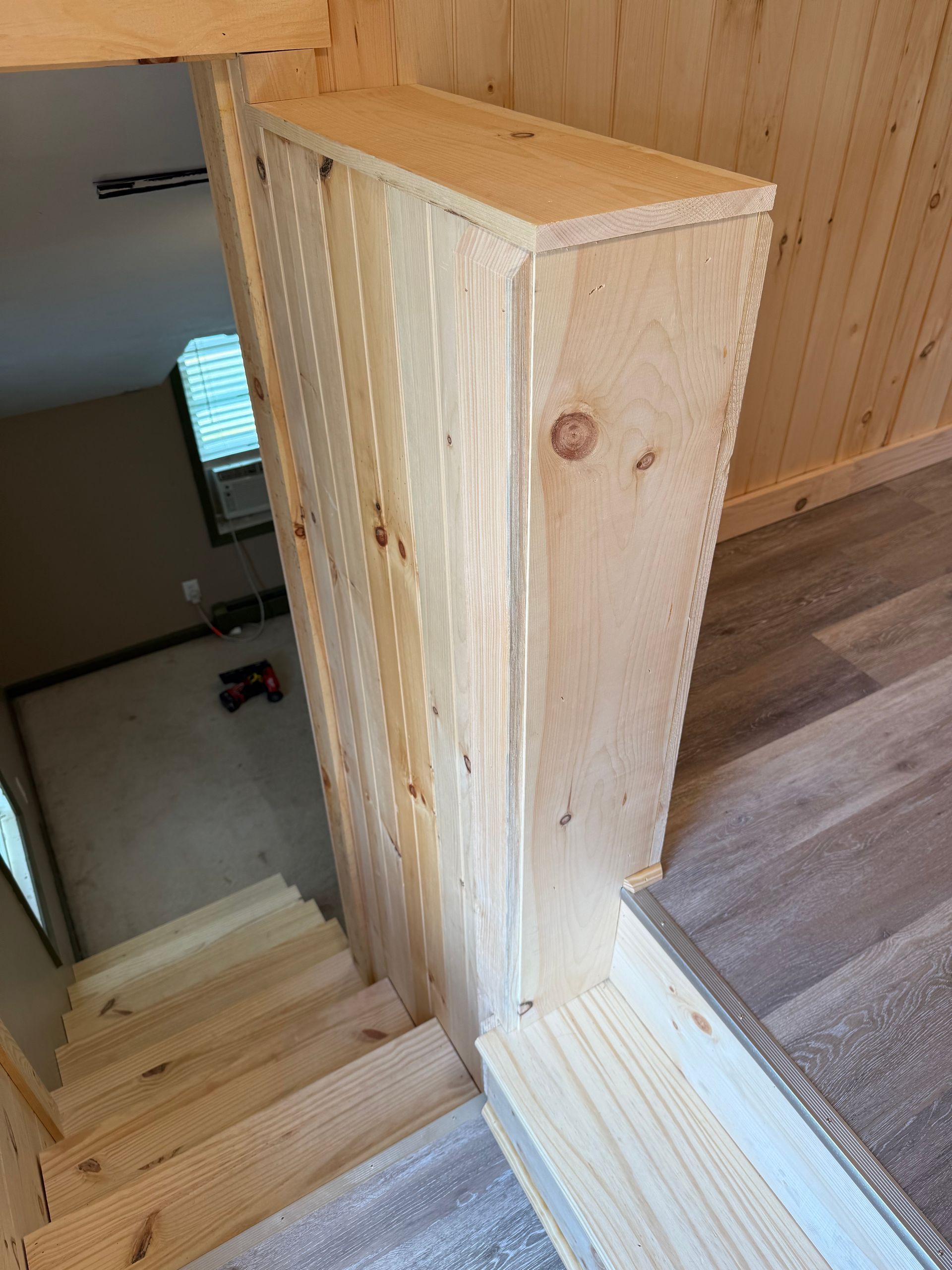 Wooden staircase with a wooden guardrail/post. Light wood paneling.
