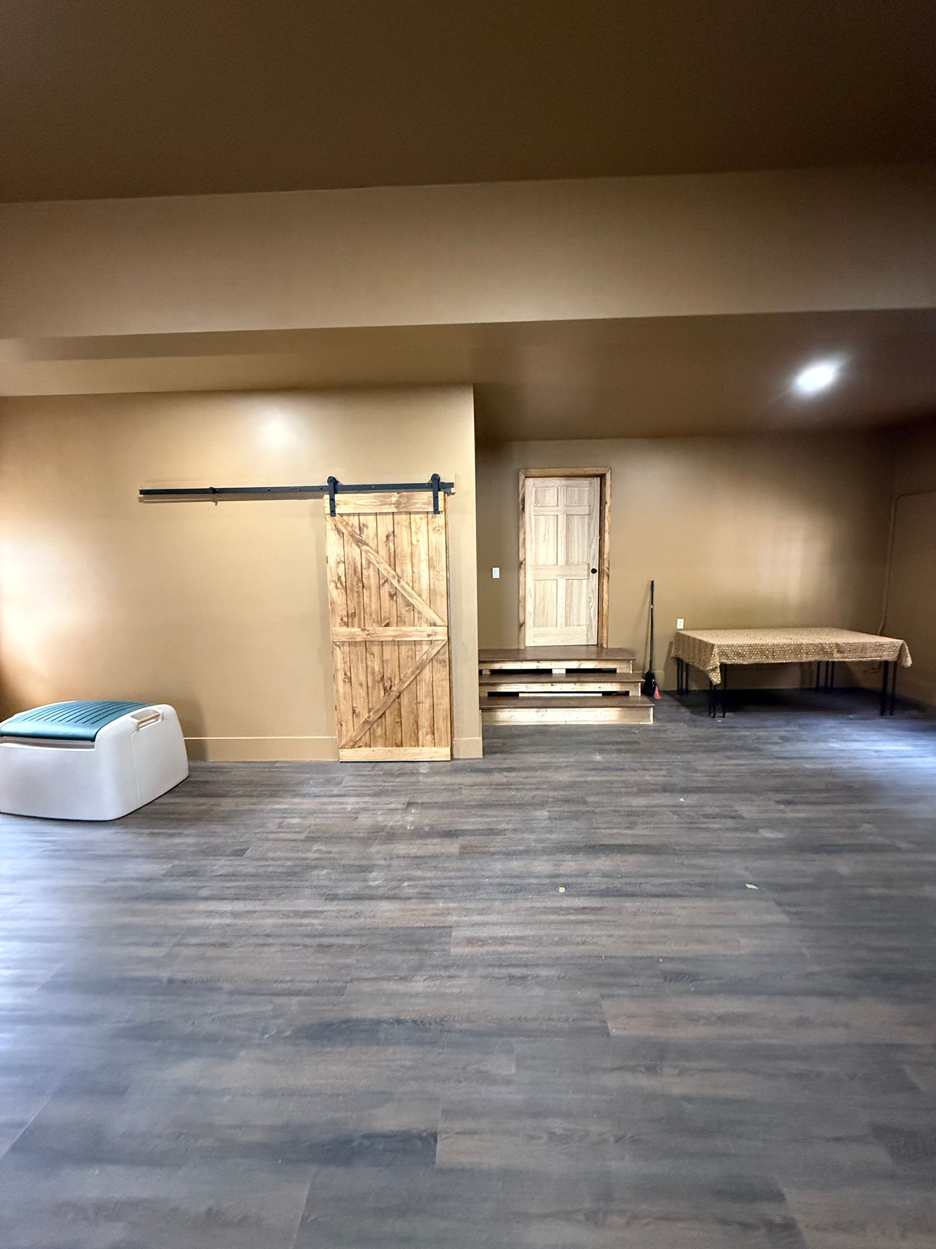 Empty room with wood flooring, tan walls, and a barn door. Table and doorway visible.