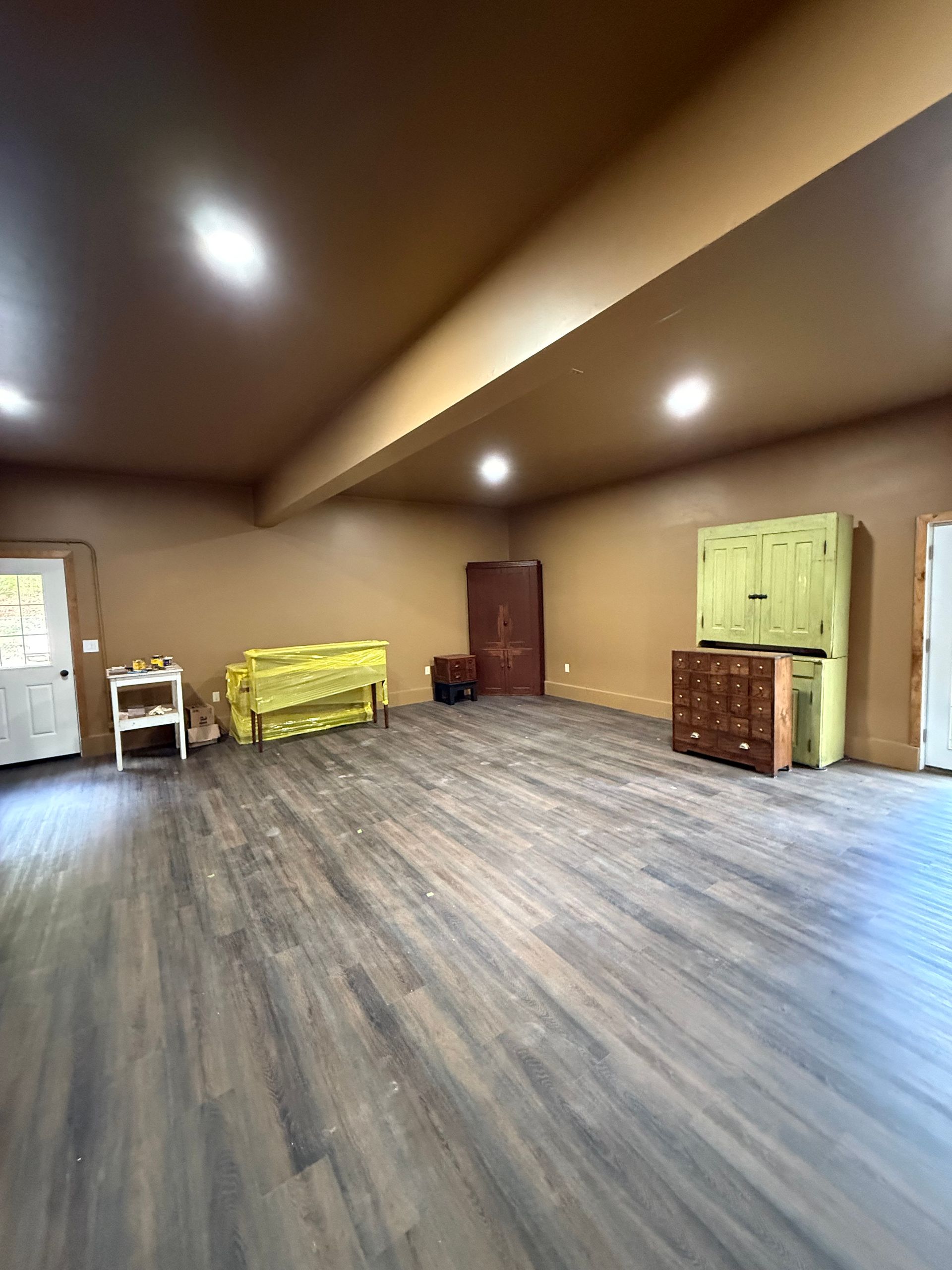 Empty room with wood-look floor, brown walls, and built-in lighting. Several pieces of furniture are present.