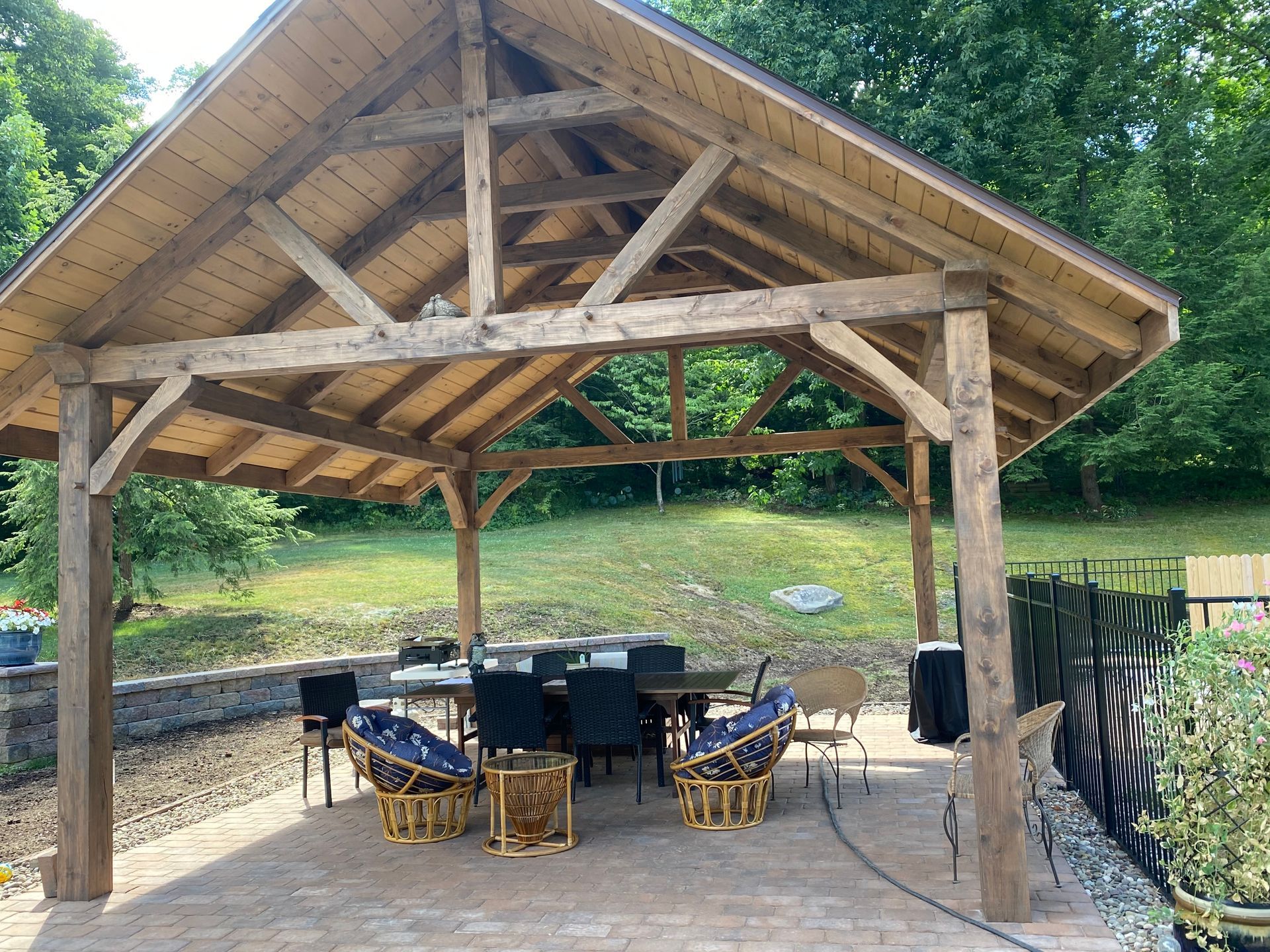 Wooden pavilion with outdoor dining table on a brick patio overlooking a grassy yard.