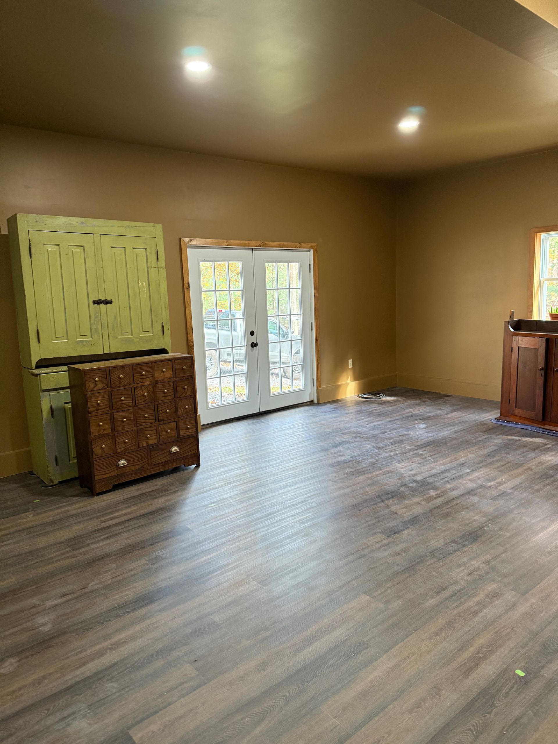 Empty room with brown walls, wood-look floor, French doors, and two cabinets.