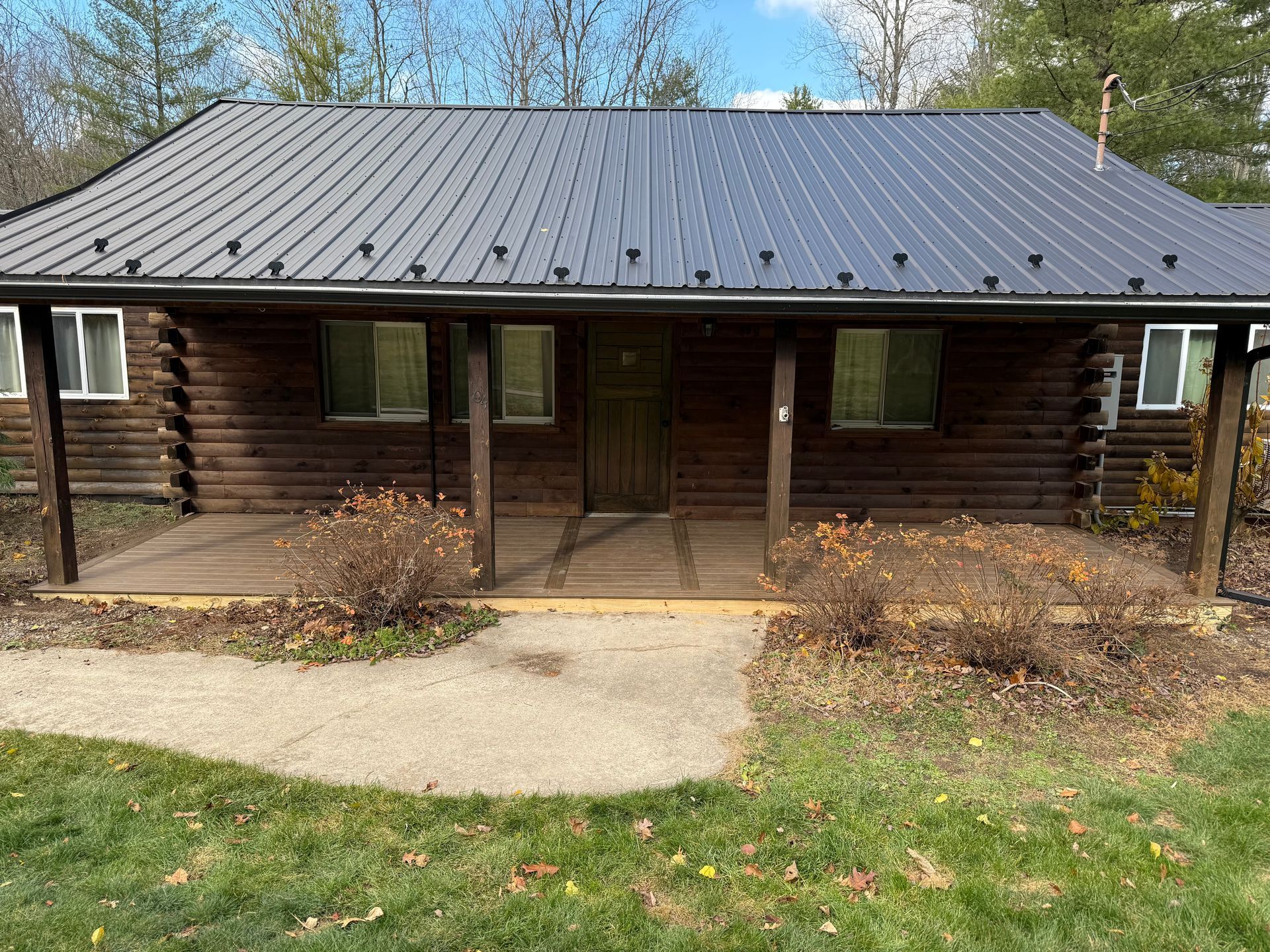 Log cabin with black metal roof, porch, and a concrete path.