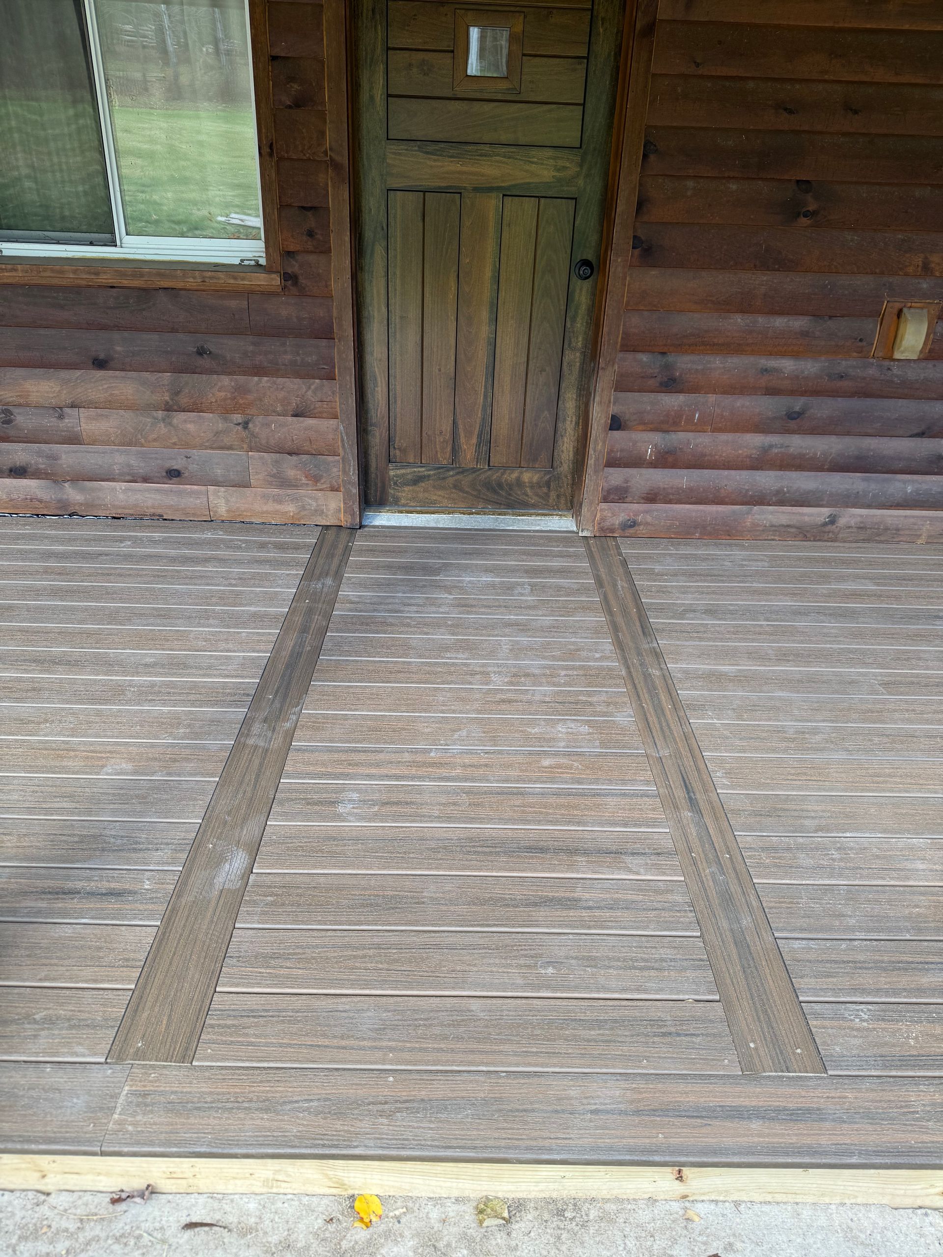 Wooden porch with a ramp leading to a weathered door, beneath a log cabin exterior.