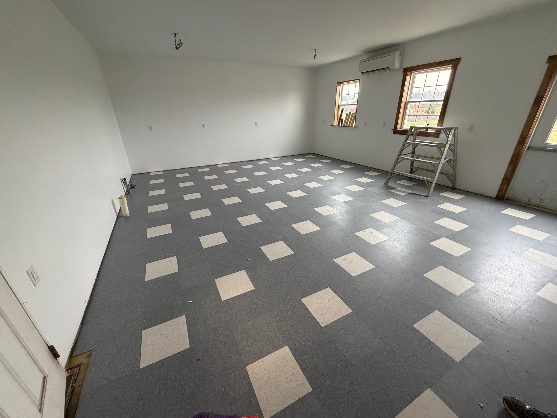 Empty room with blue and white checkered floor, white walls, and a ladder.