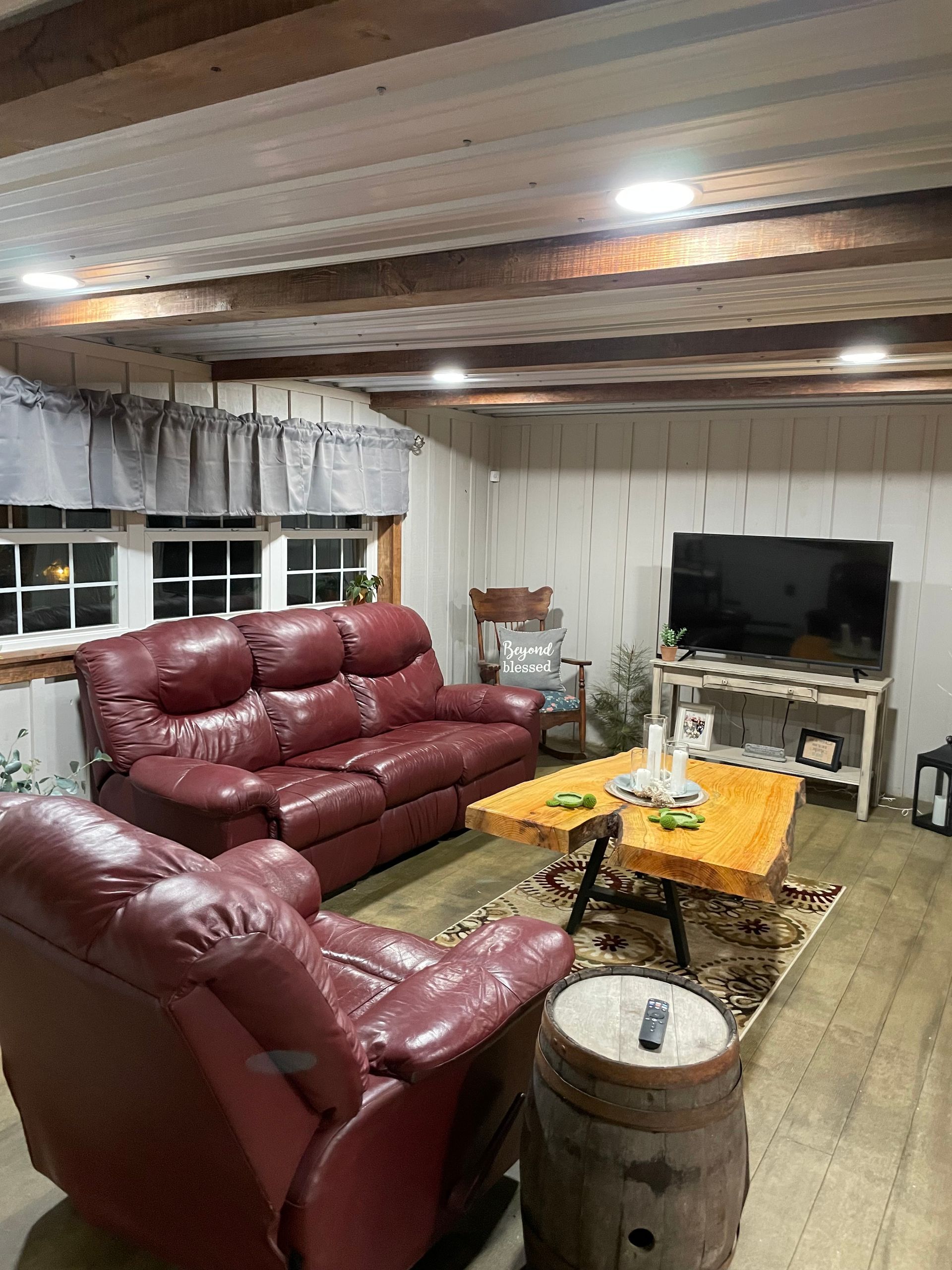 Living room with red leather furniture, wood coffee table, TV, and exposed wood beams.