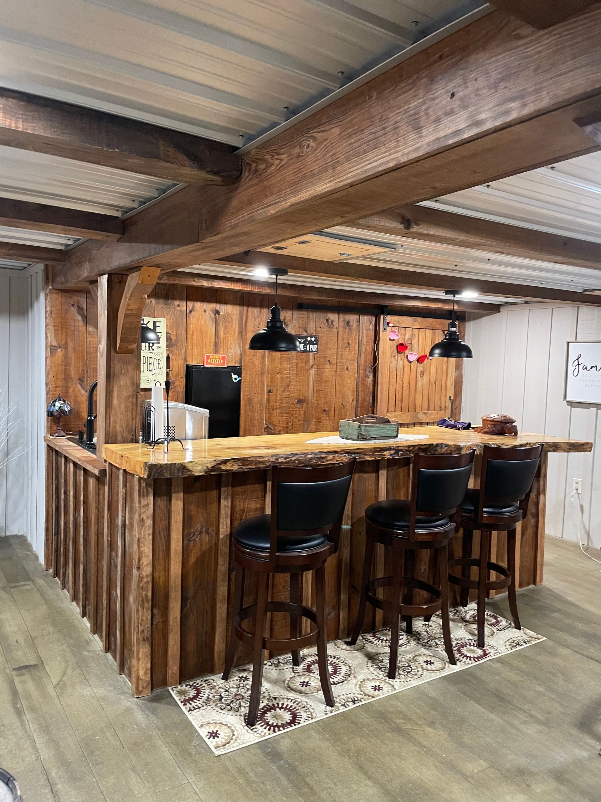 Rustic bar with wood counter, stools, and pendant lights. A small rug is on the floor.
