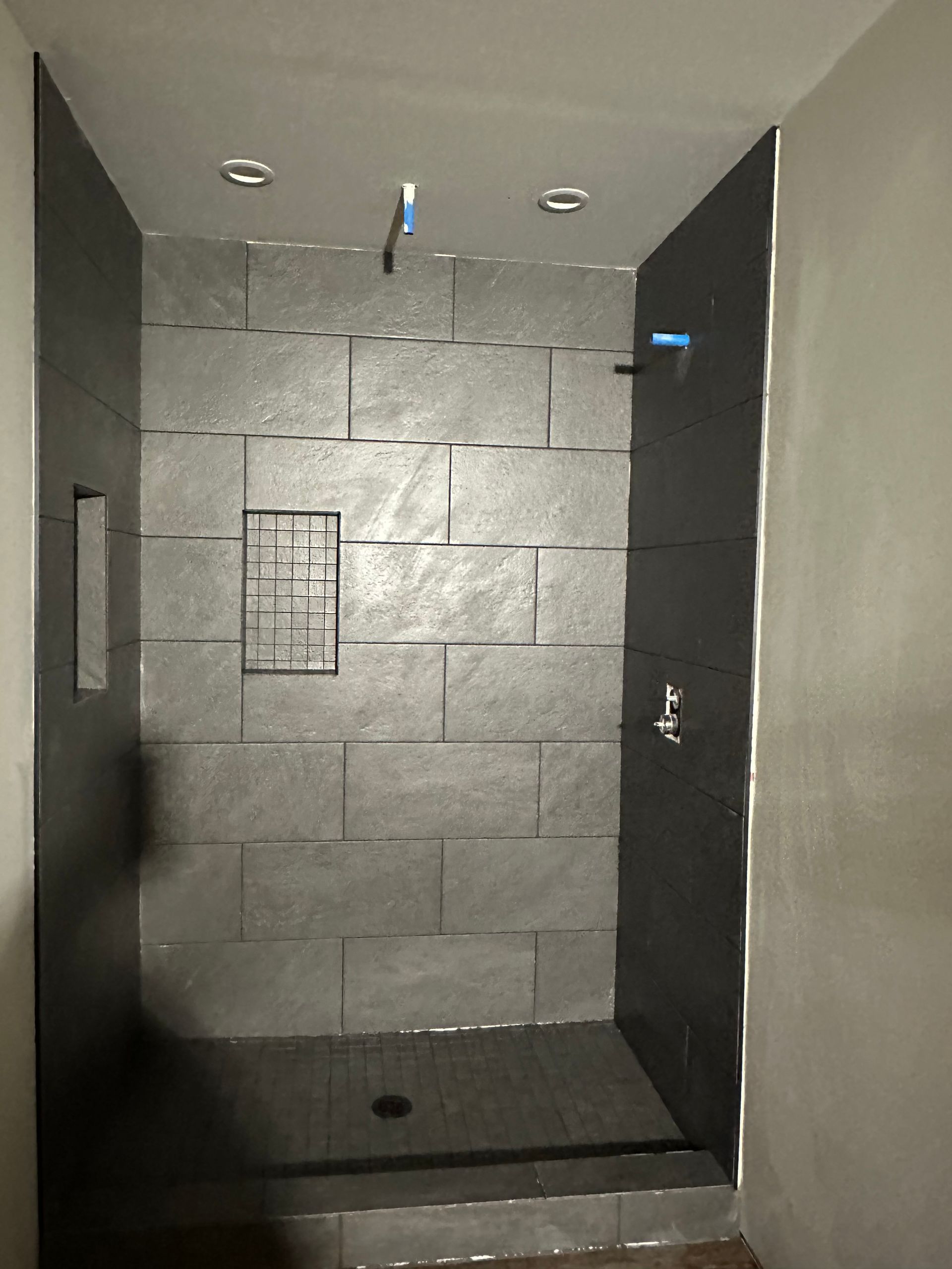 Gray tiled shower under construction, with fixtures and recessed lighting.
