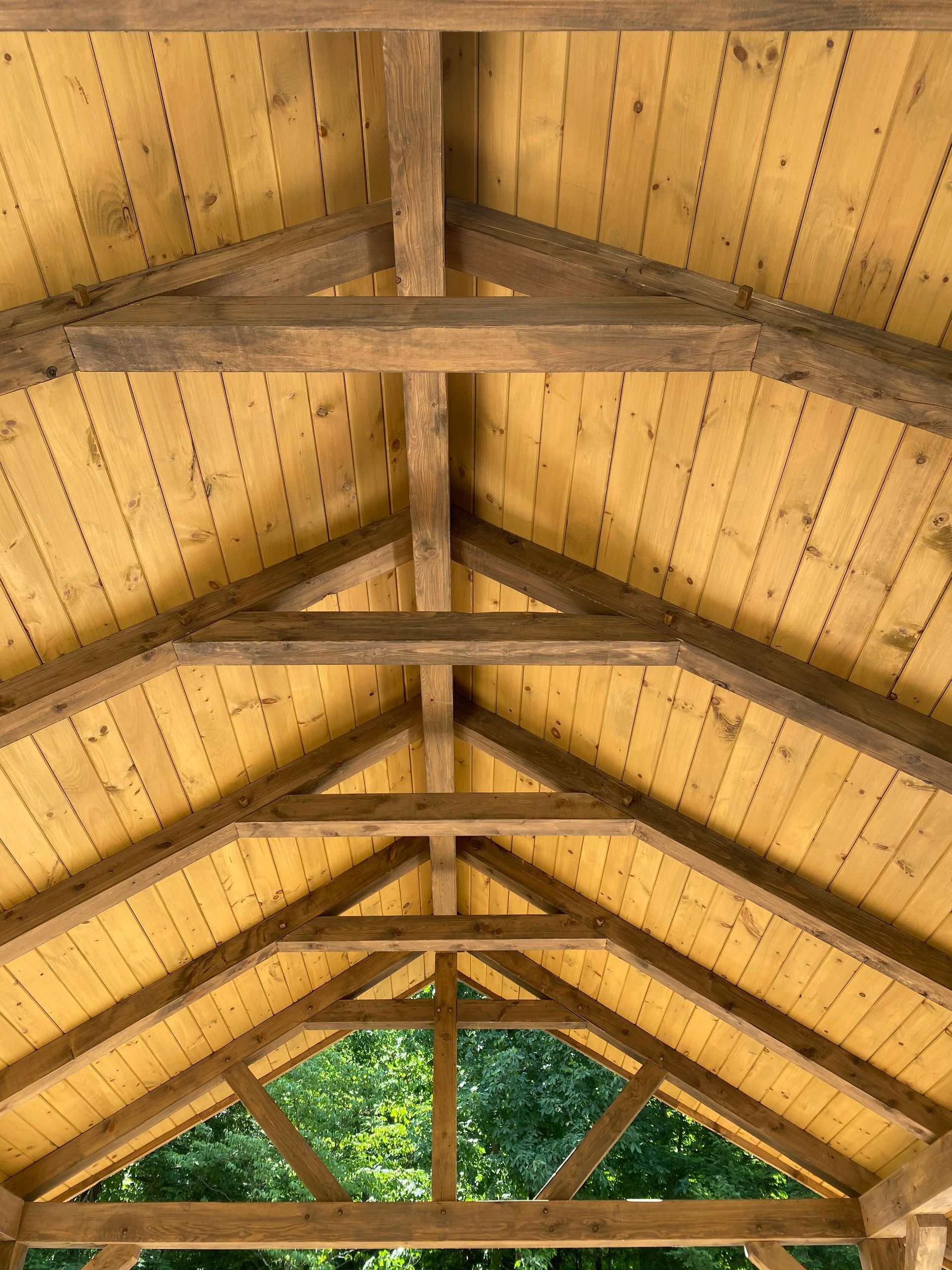 Wooden roof framing with exposed beams and ceiling planks, viewed from below.