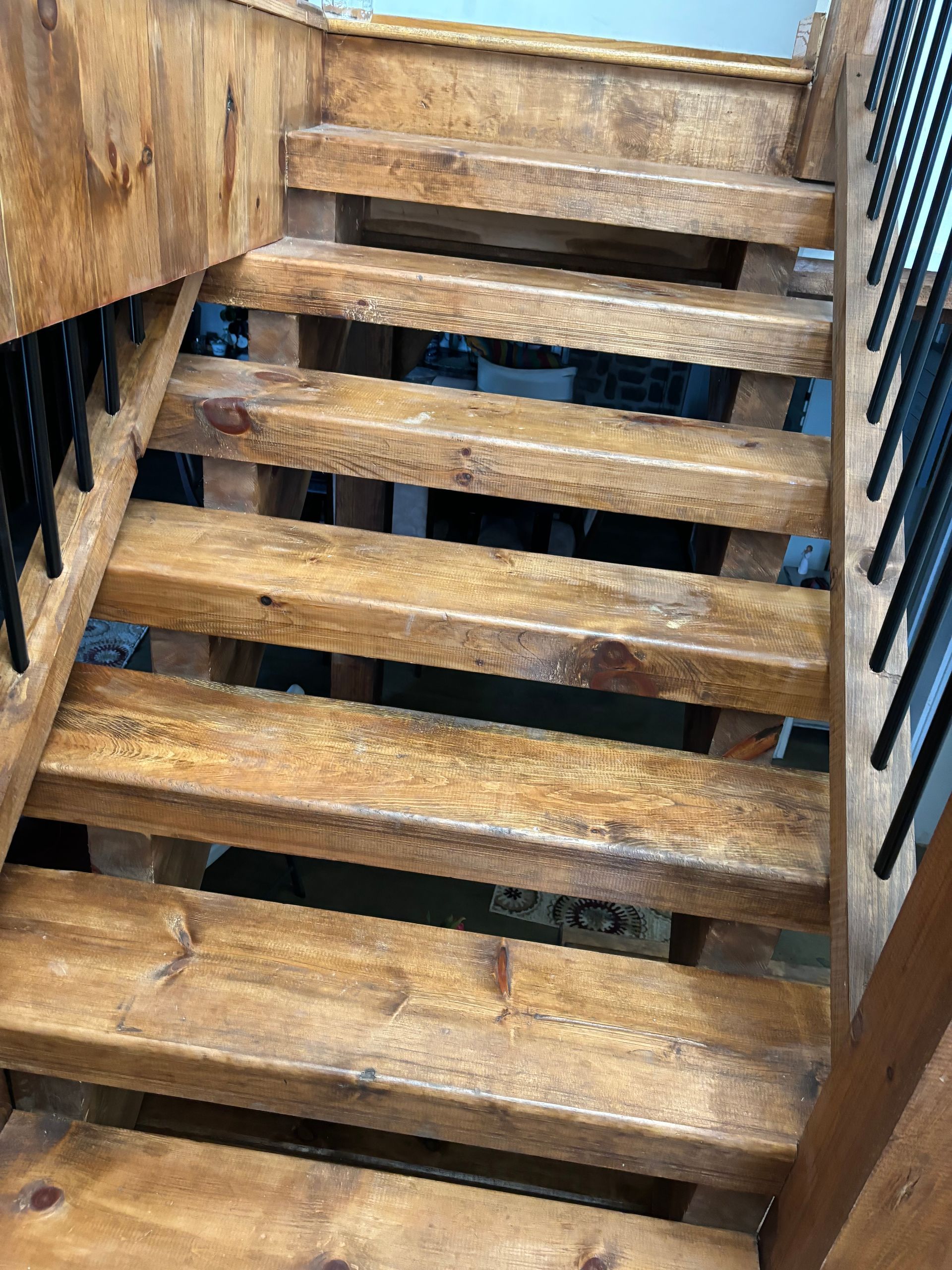 Wooden staircase with open risers and black metal railings.