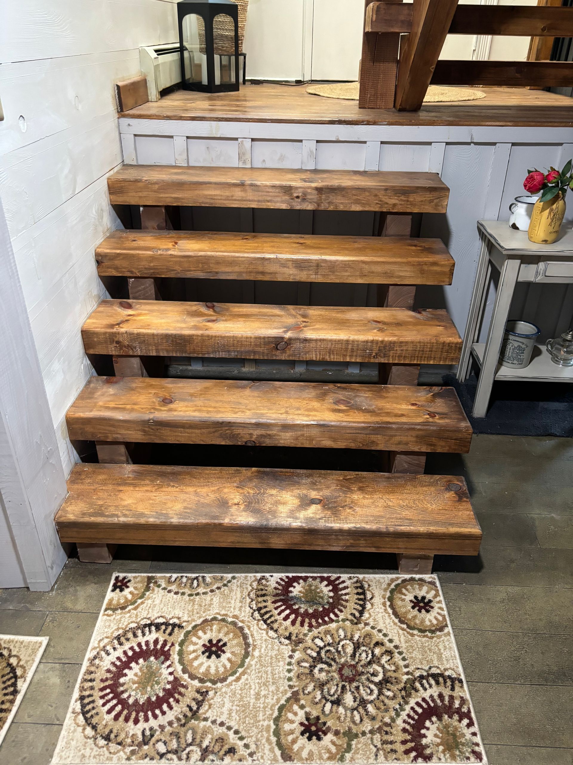 Wooden stairs leading up, with a patterned rug at the bottom, and a small table on the right.