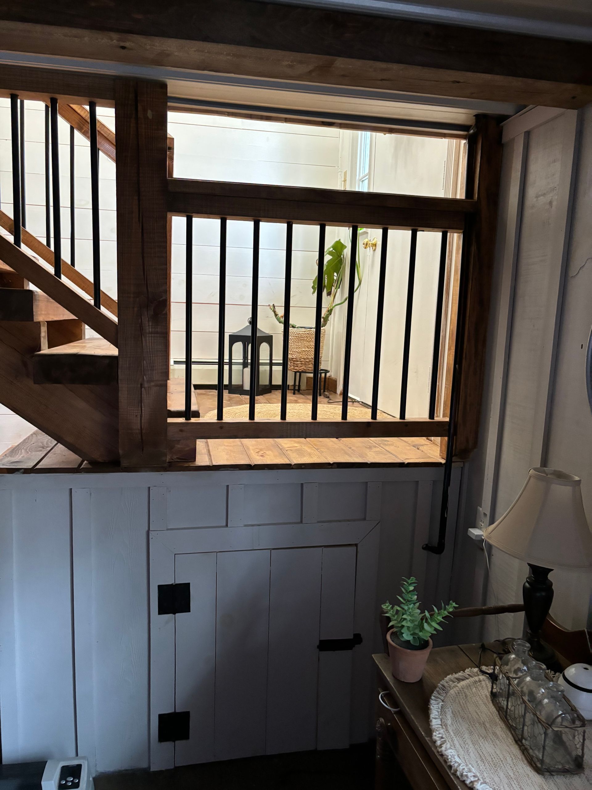 Wooden staircase leads to a barred window overlooking a small courtyard with greenery.