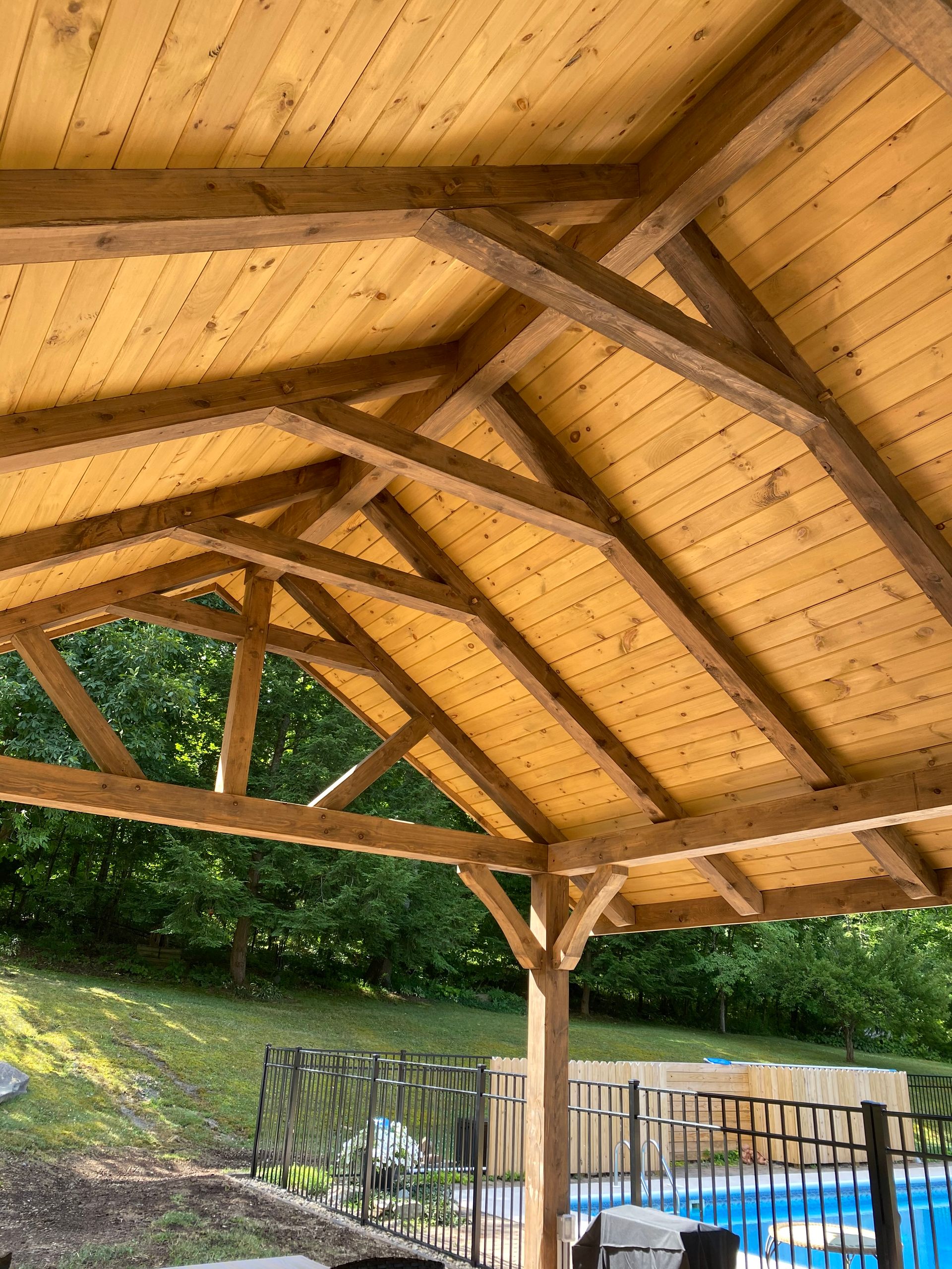 Wooden gazebo roof structure with rafters, panels, and supports over a pool area.