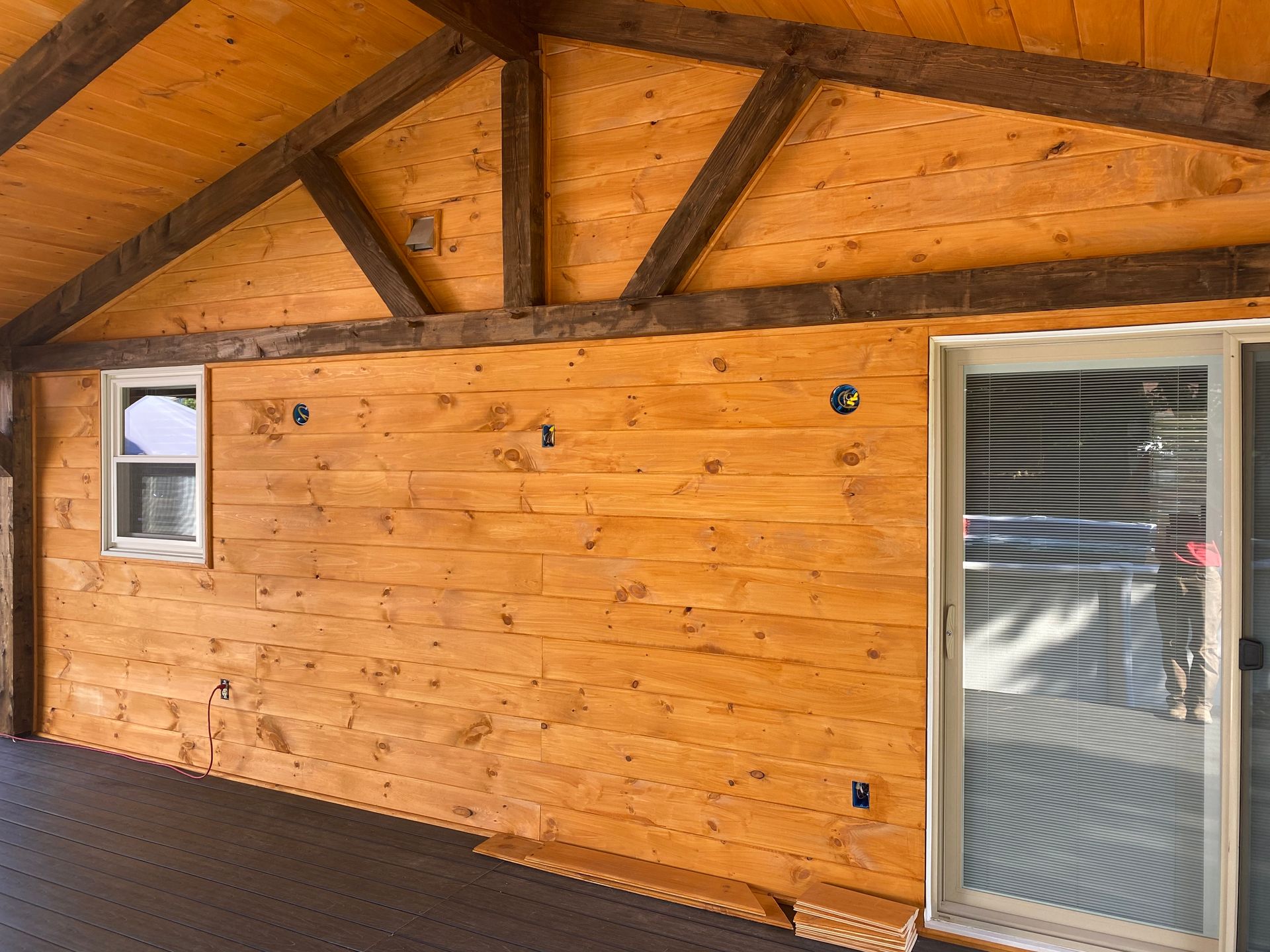 Wooden porch with wood-paneled ceiling and walls. Window, sliding glass door, and dark wood flooring.