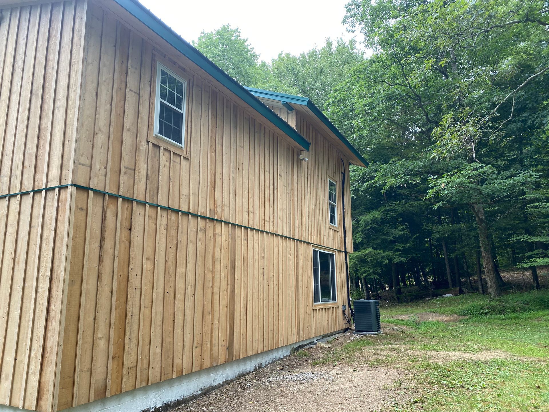 Wooden cabin with green roof and windows, surrounded by trees.