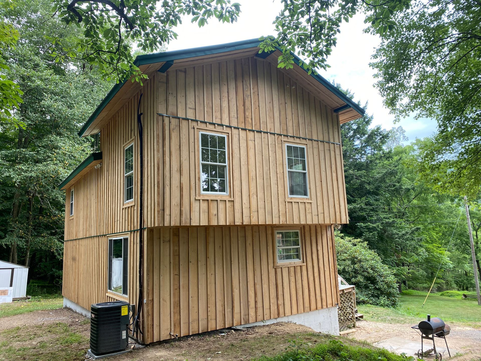 Two-story wood-sided cabin with green roof and multiple windows, surrounded by trees.