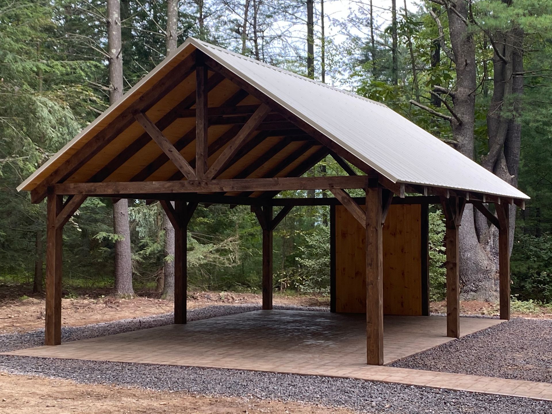 Wooden carport with metal roof in a wooded area.