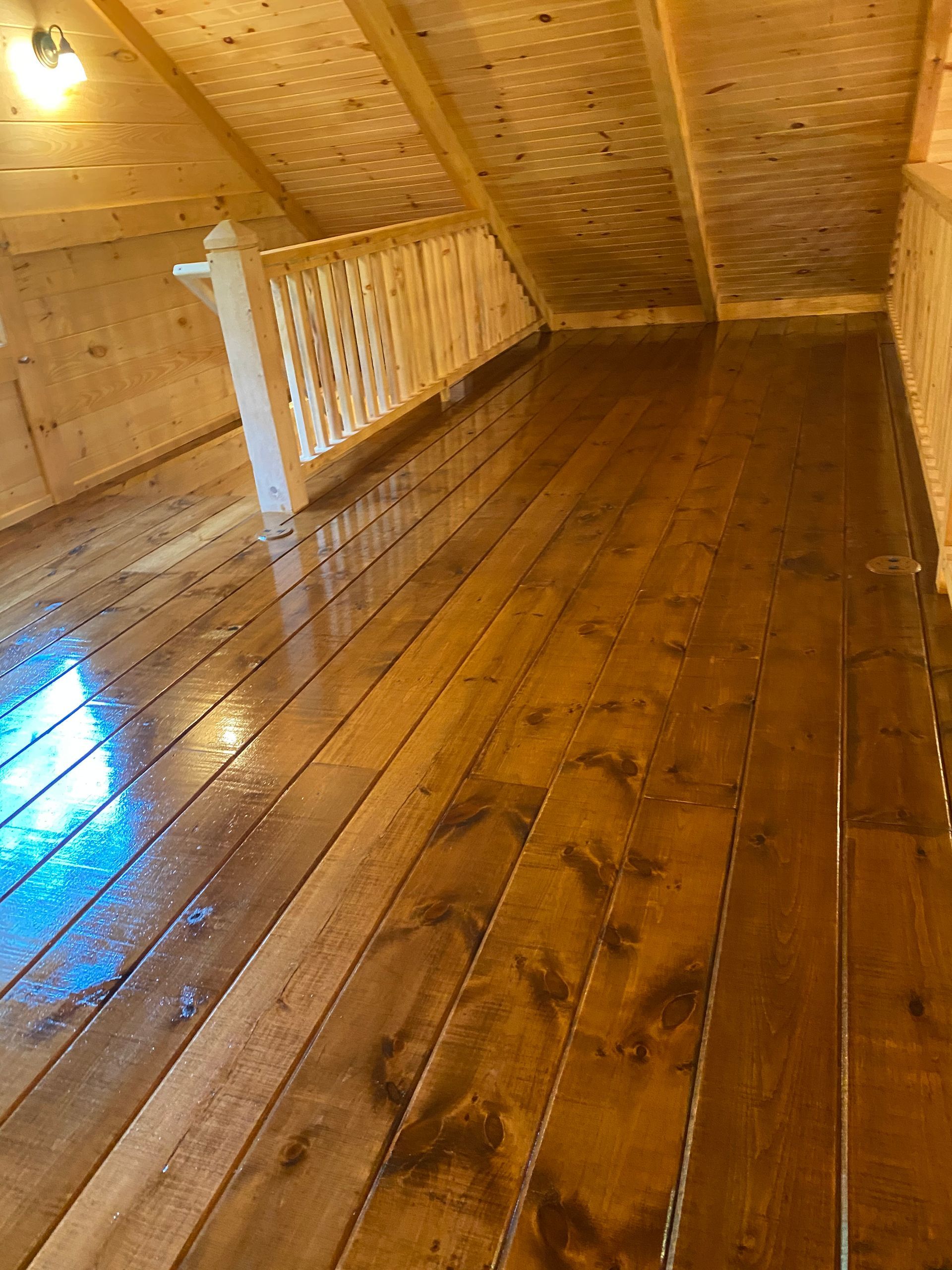 Wooden attic room with wood plank floor and sloped ceiling. A white railing is visible.