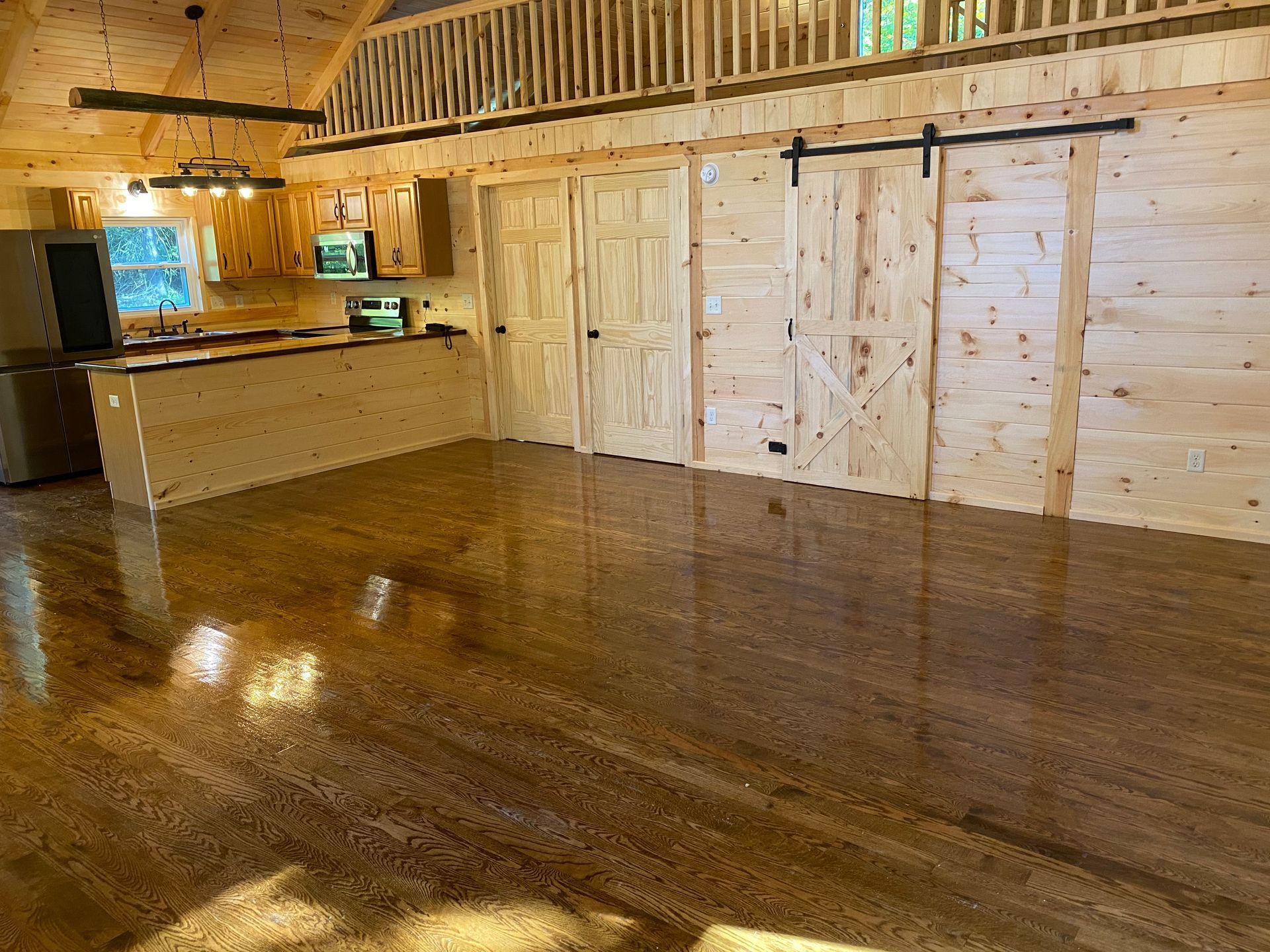Interior of a cabin with wooden walls, floors, and a kitchen area. Sliding barn doors and loft visible.