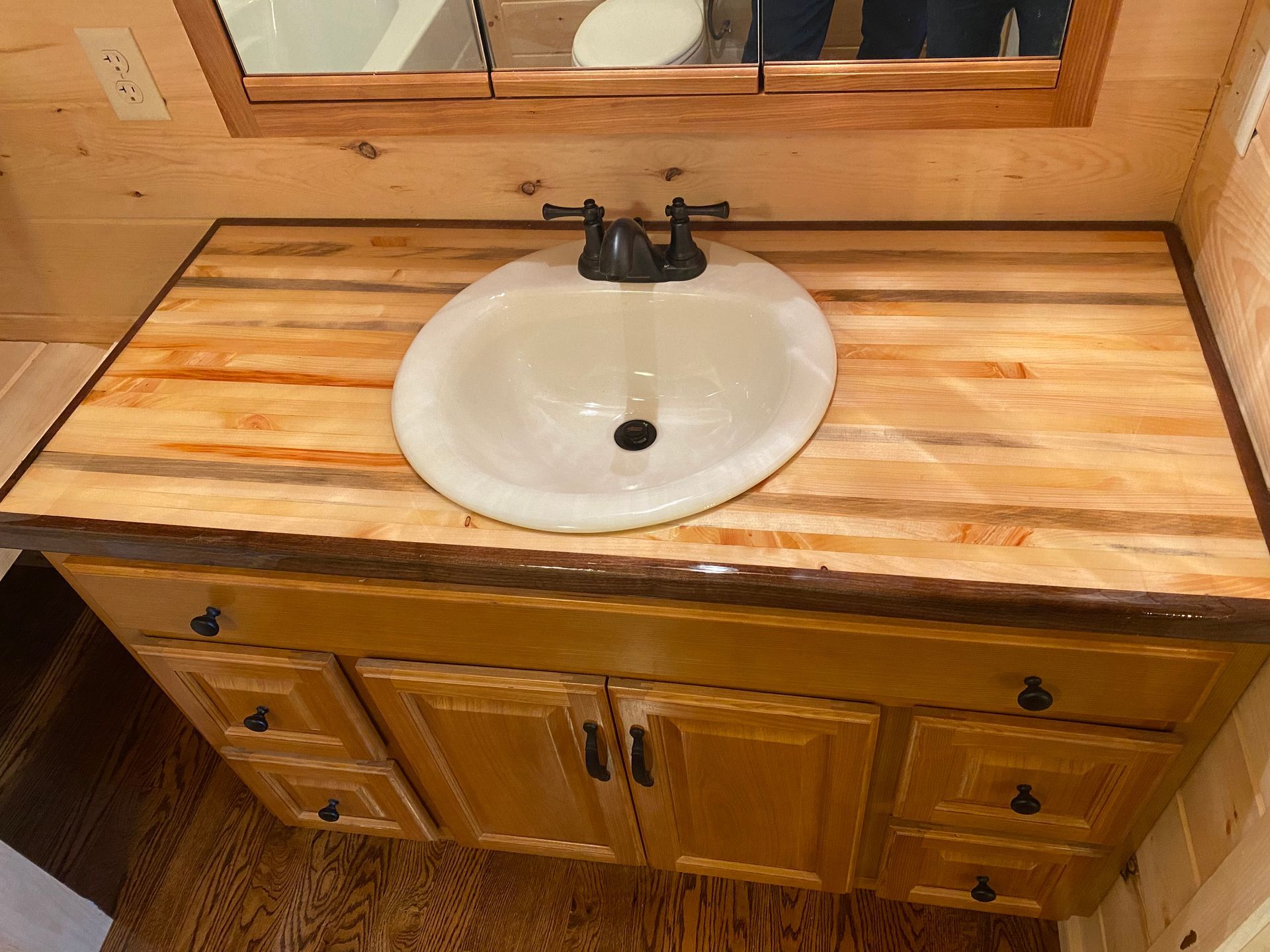 Bathroom vanity with light wood countertop, white sink, and brown cabinets.