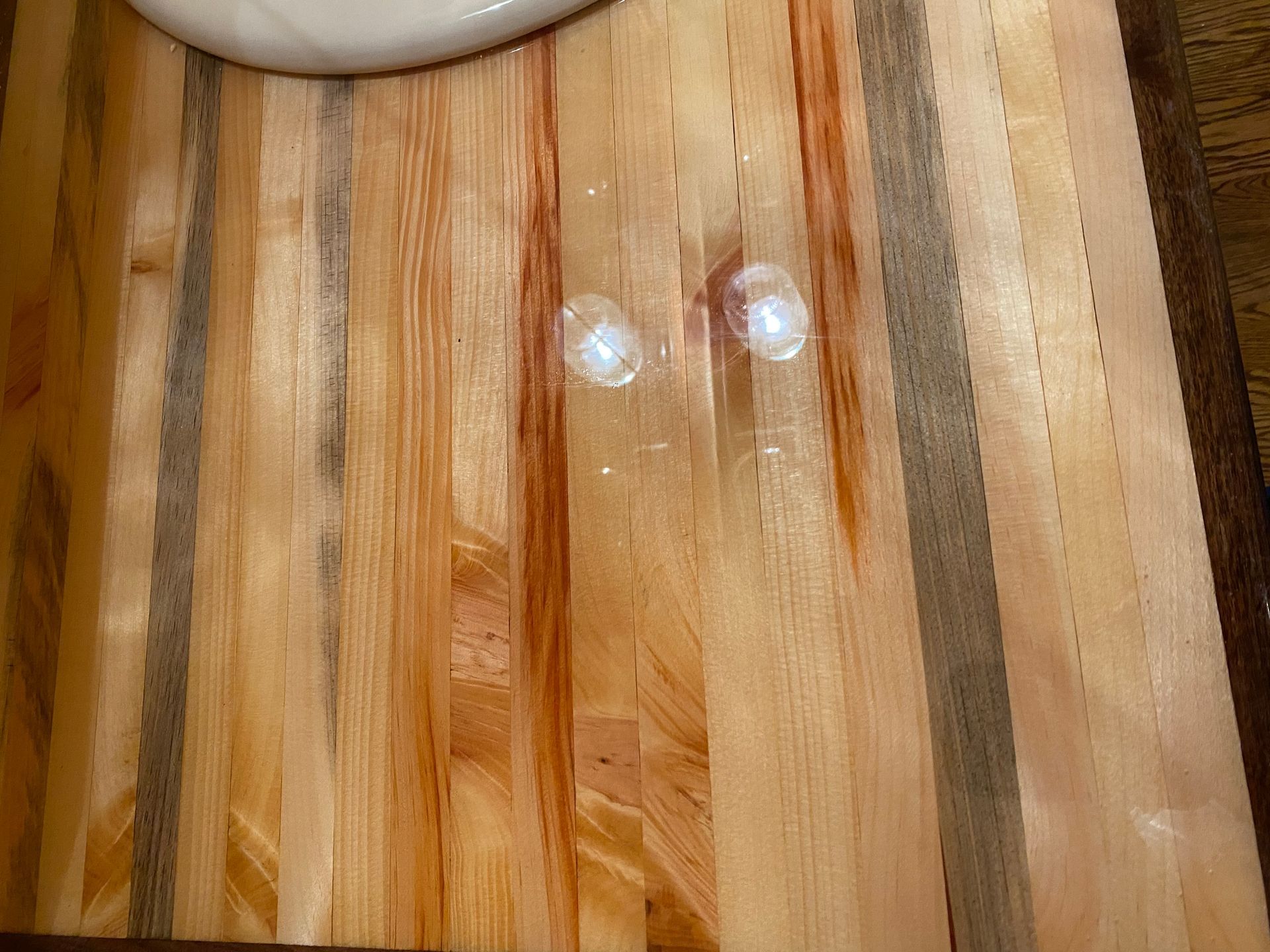 Two ice cubes melting on a wood cutting board, next to a white ceramic object.