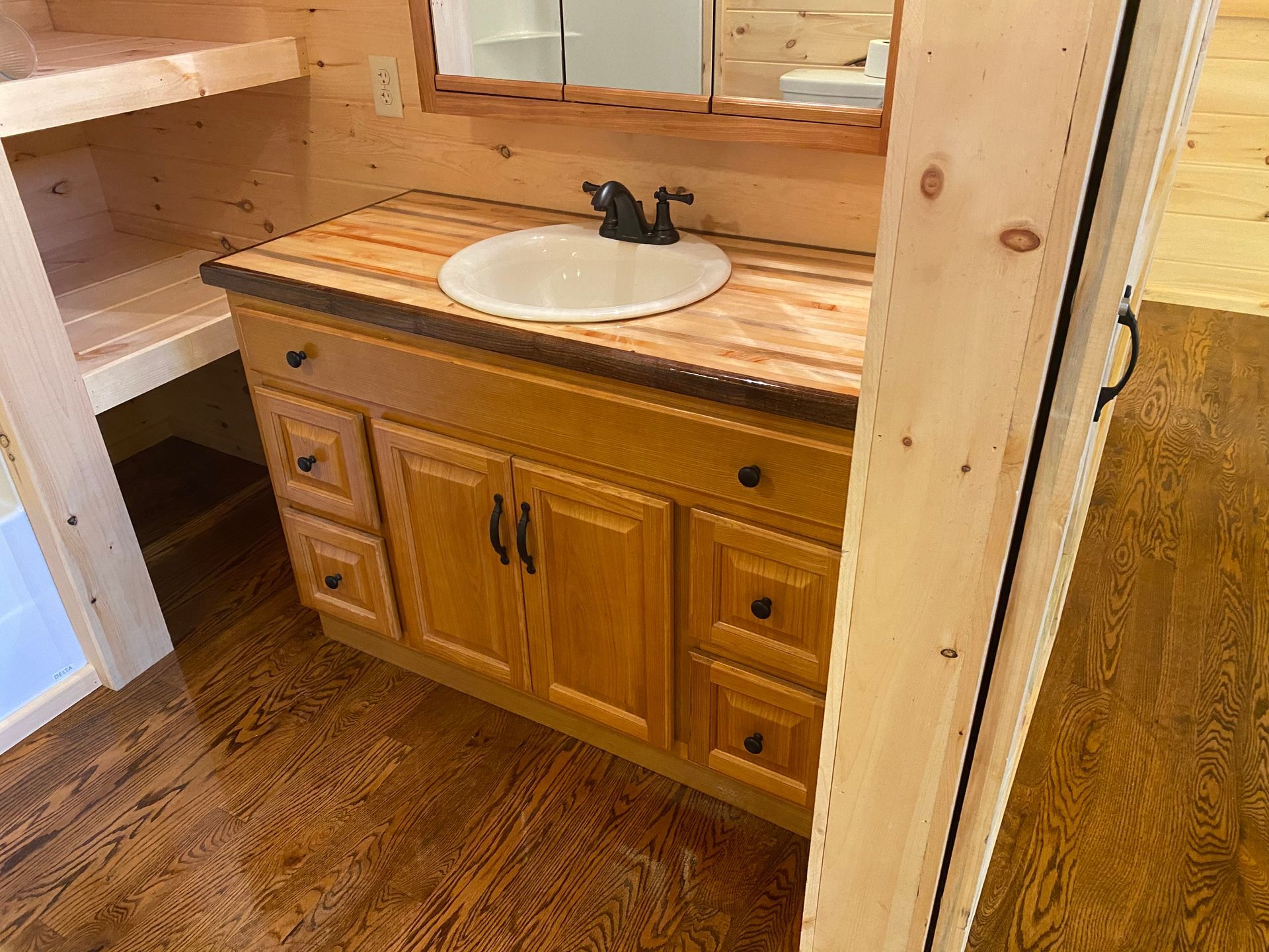 Bathroom vanity with light wood cabinets, dark faucet, and a round sink.