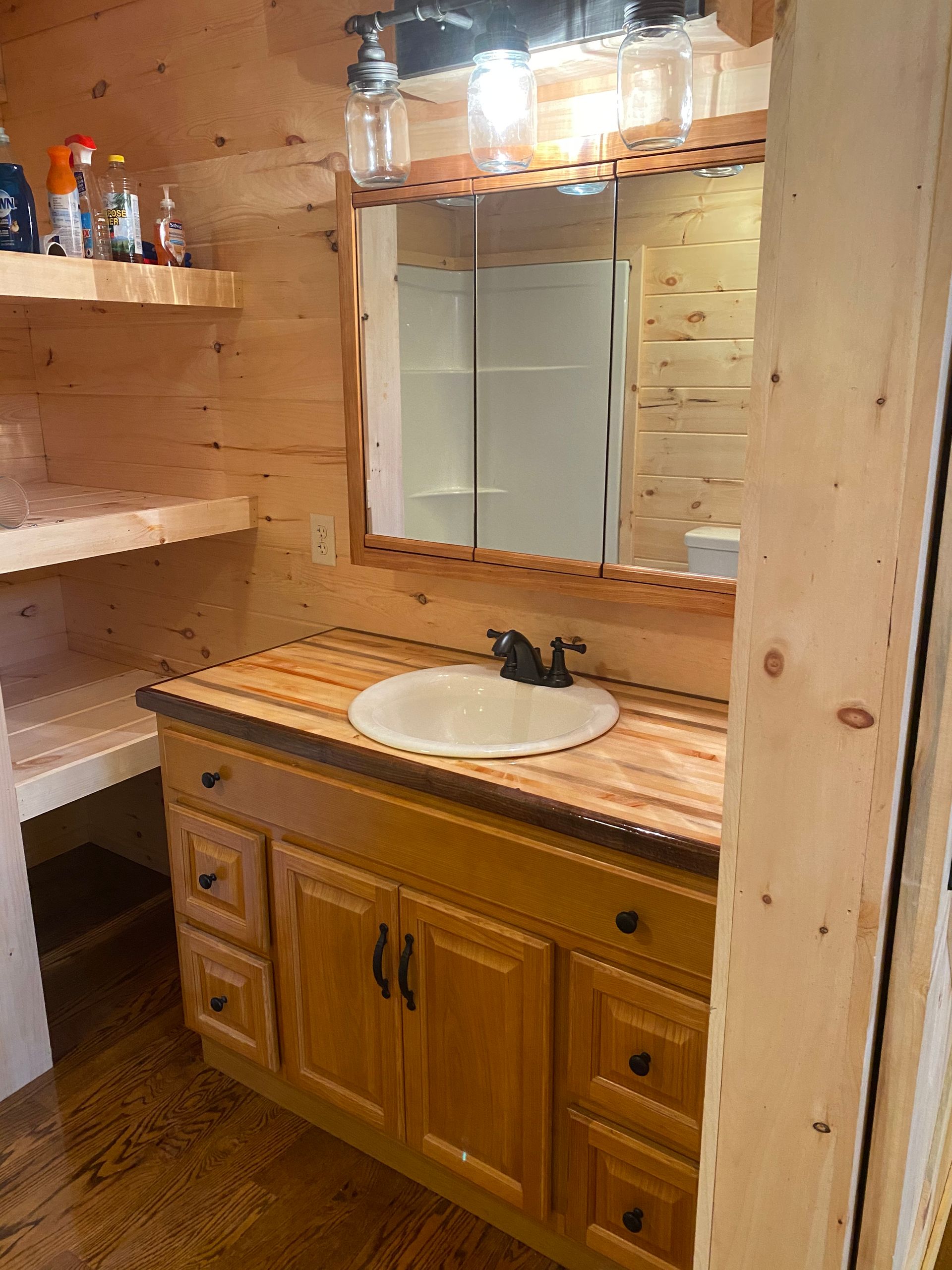 Bathroom with wooden vanity, sink, mirror, and shelves.
