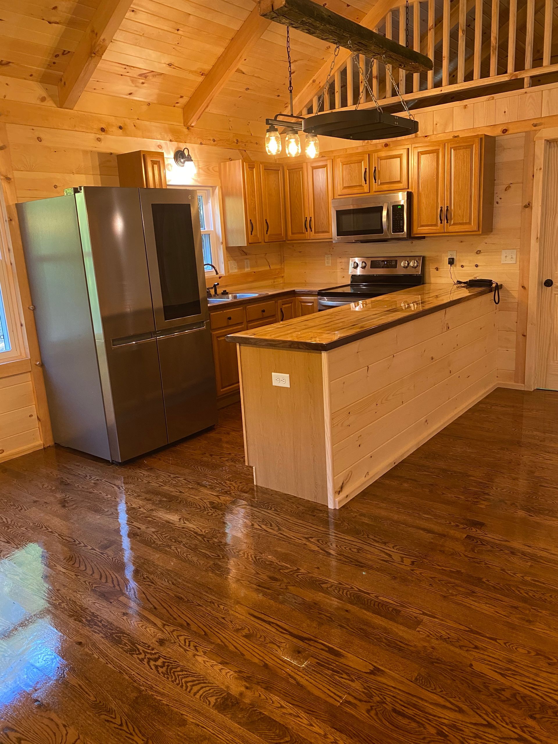 Kitchen with wooden cabinets, island, and stainless steel appliances. Shiny brown floor.