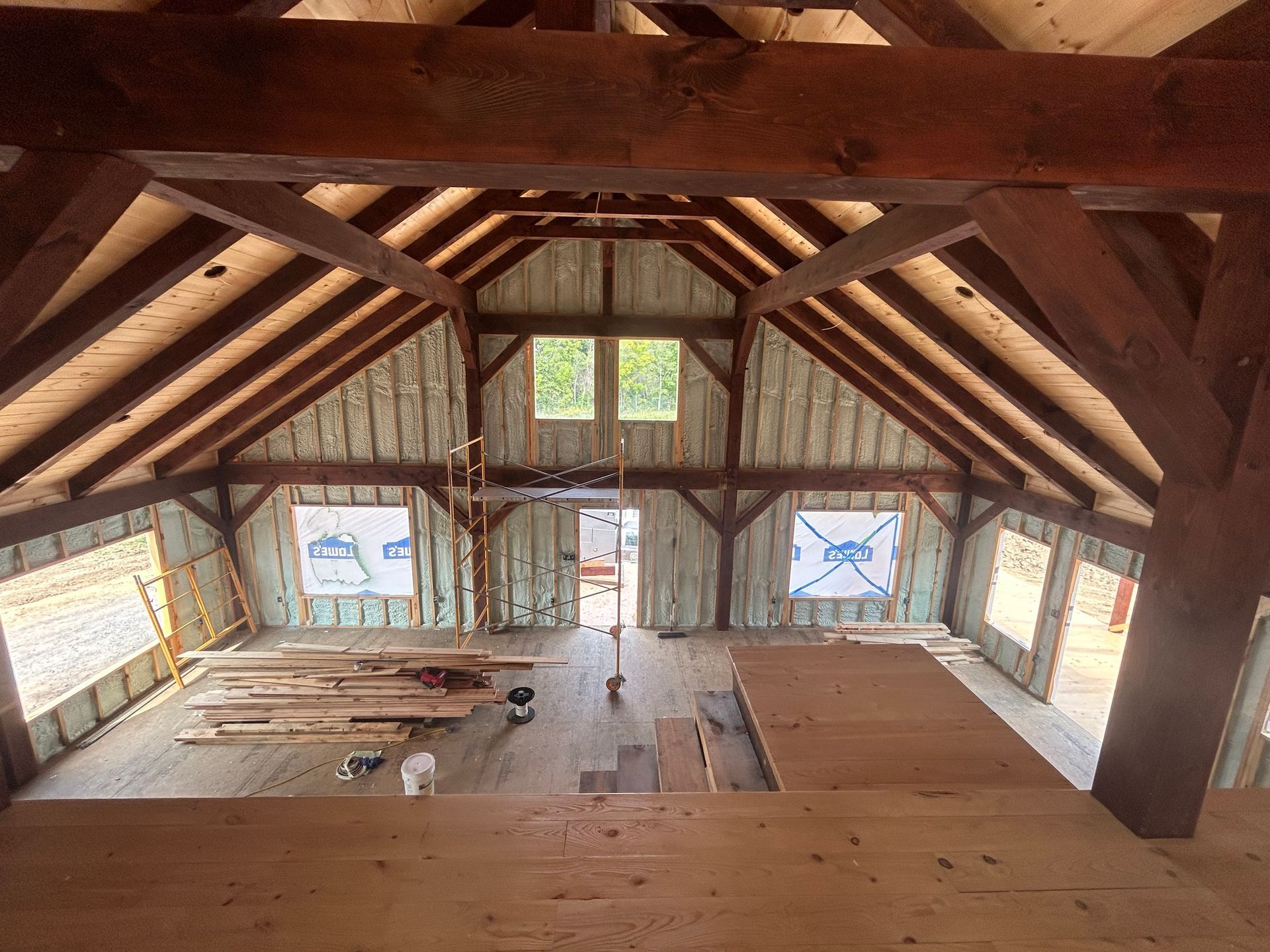 Interior view of a wooden building under construction, showing framing, windows, insulation, and lumber.