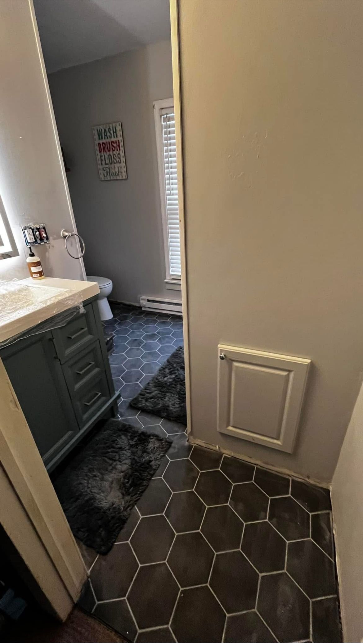 Bathroom with blue vanity, gray hexagon tile floor, and a vent cover on the wall.