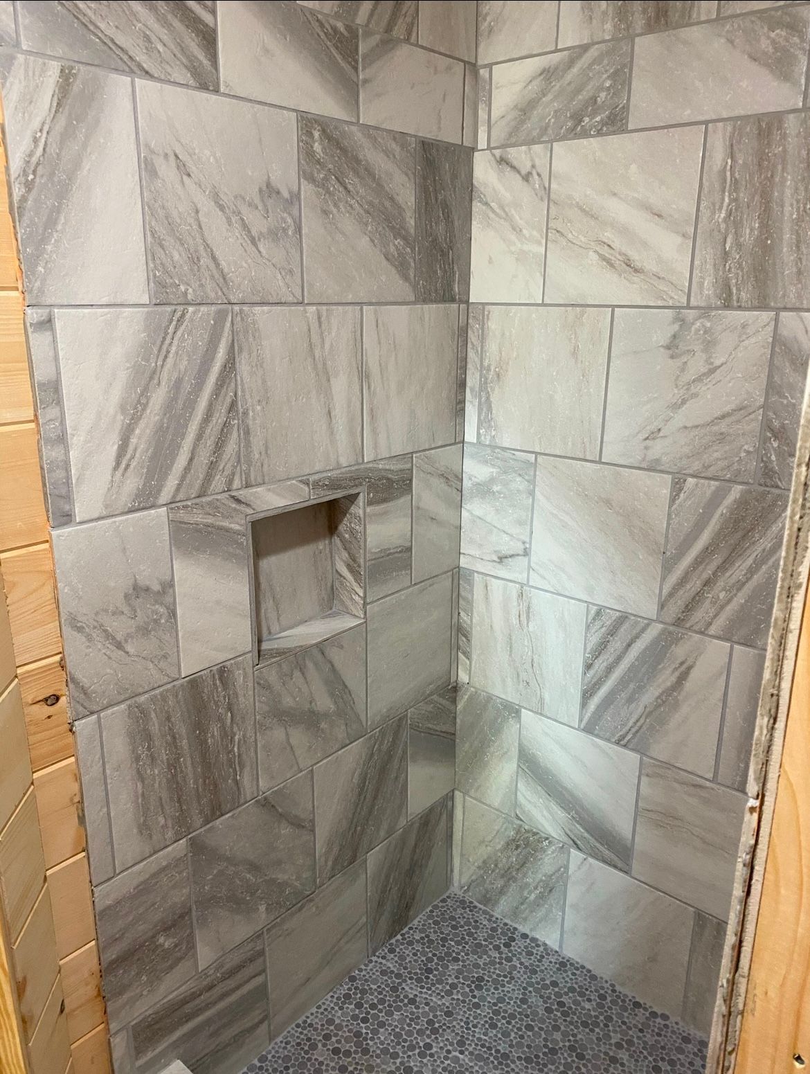 Tiled shower corner with a built-in shelf. Gray and white marble-look tiles.