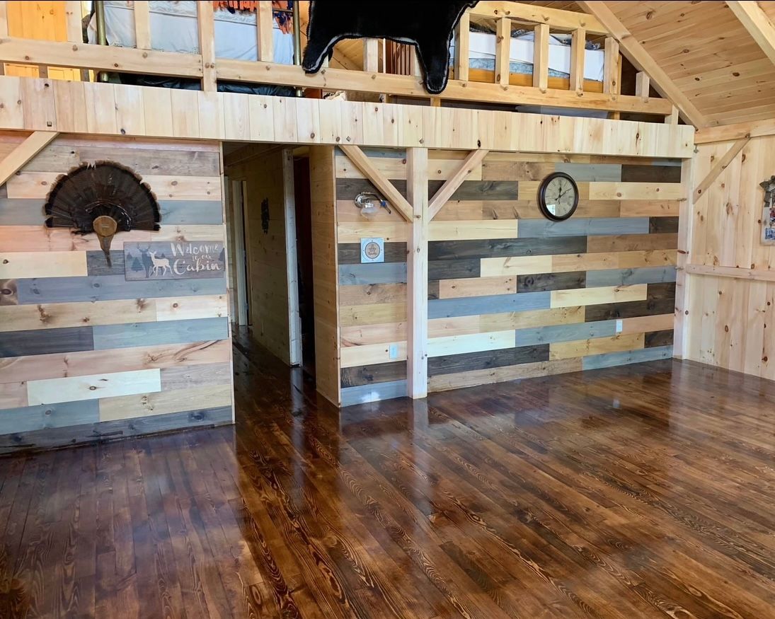 Rustic interior with wood walls and floor, loft area, decorative turkey fan, clock, and black object hanging.