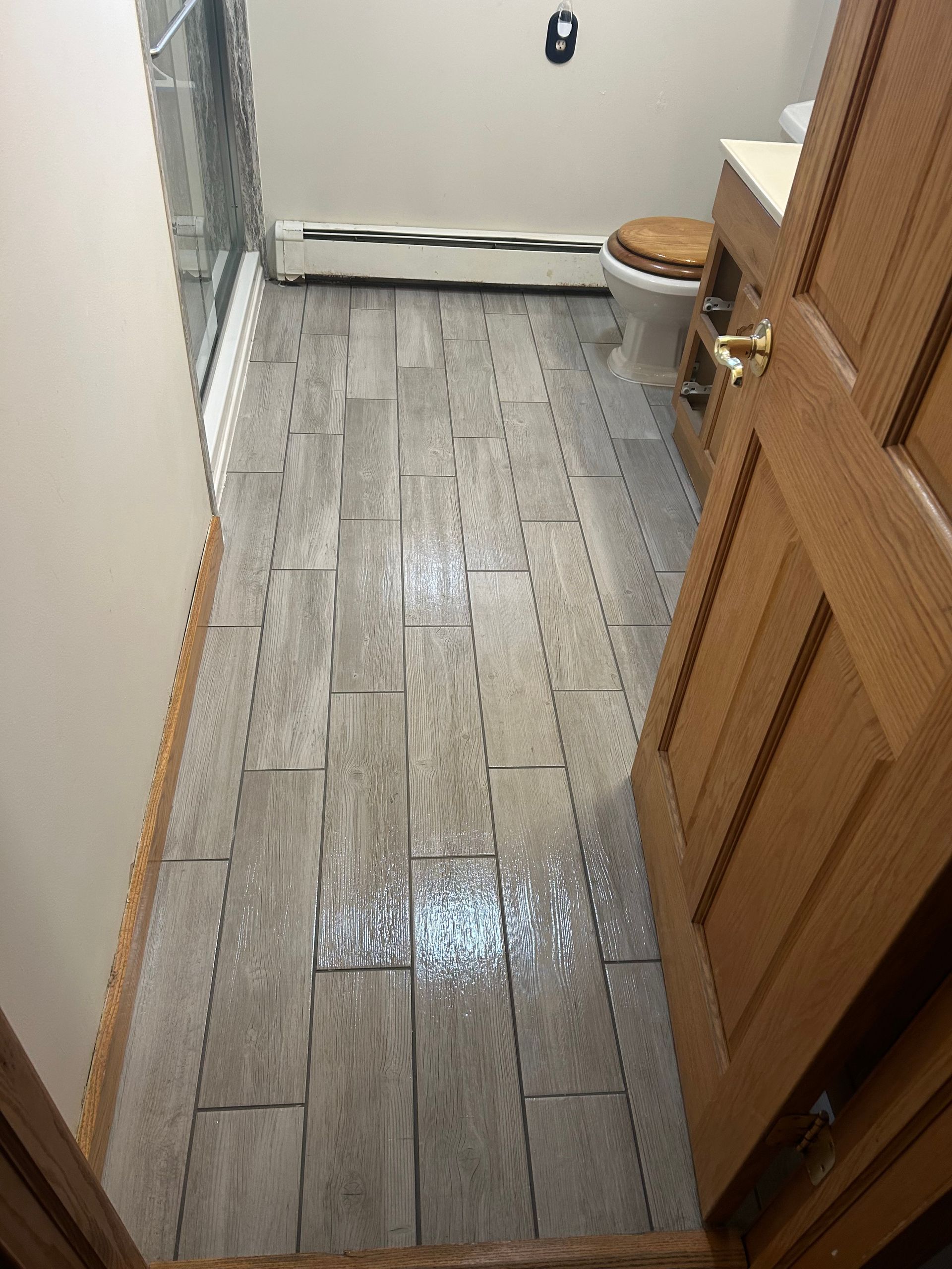 Bathroom with gray tile floor, toilet, wood door and vanity.