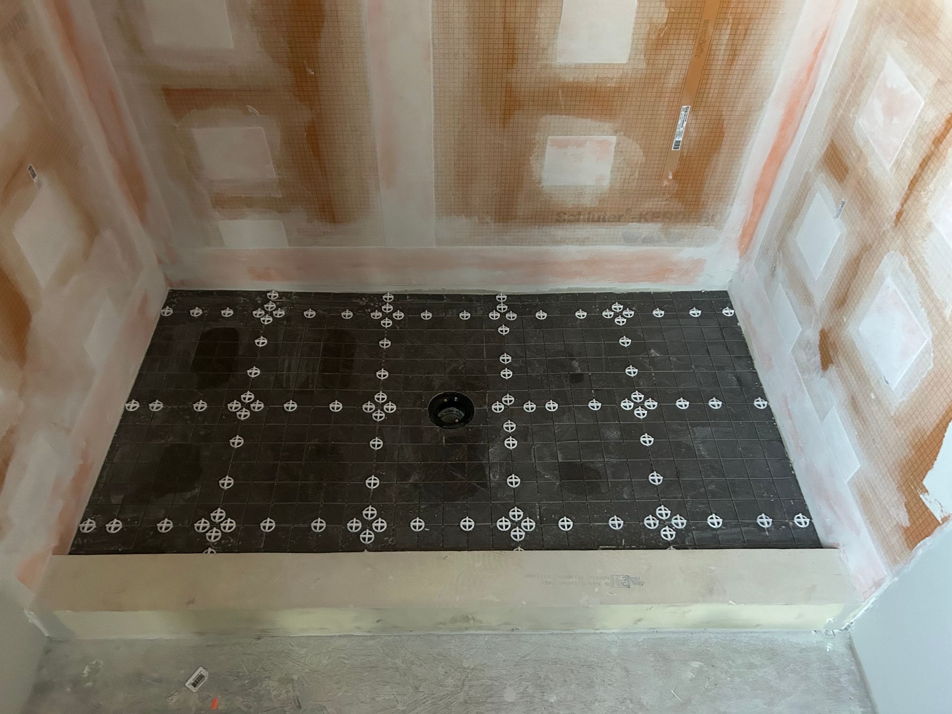 Shower stall in progress, tiled floor with leveling spacers, bare walls.