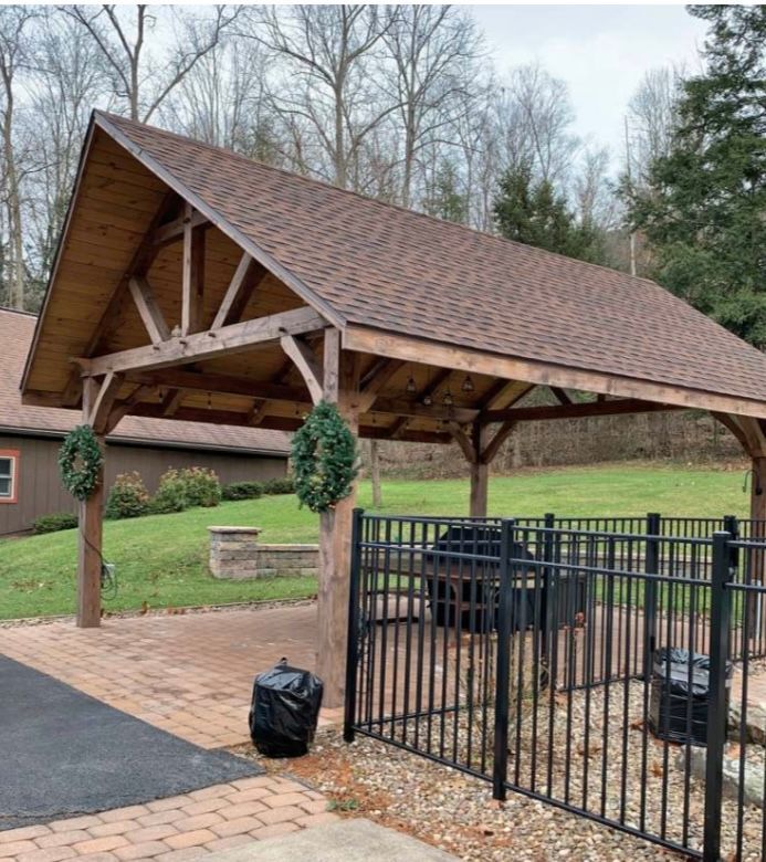 Wooden pavilion with brown roof and black fence, over a brick patio with two trash cans.