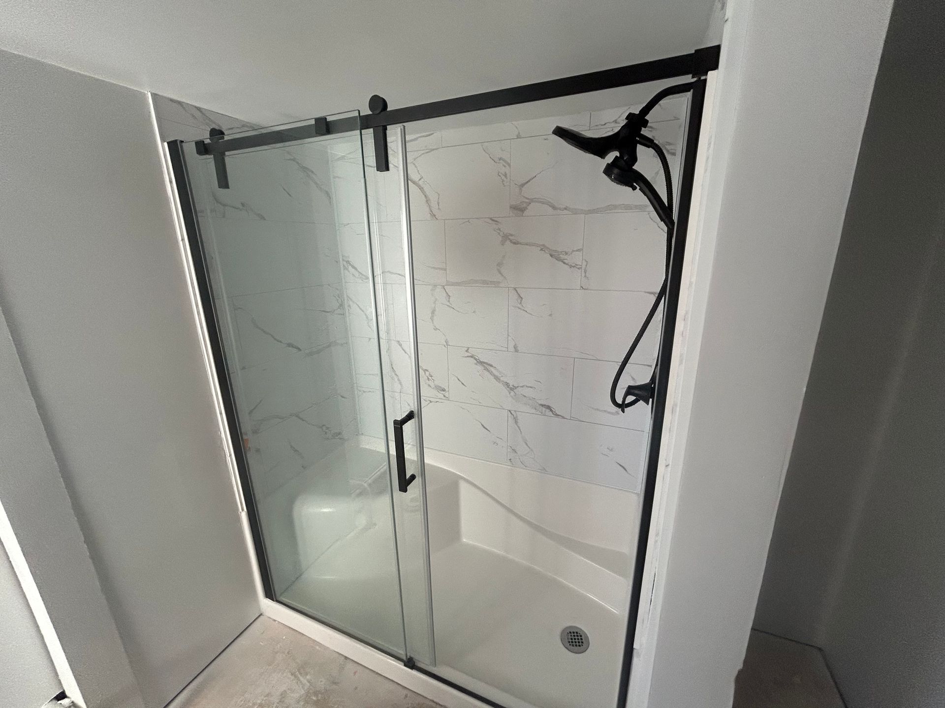 Modern shower with black frame, glass doors, white marble-look walls, and black fixtures.