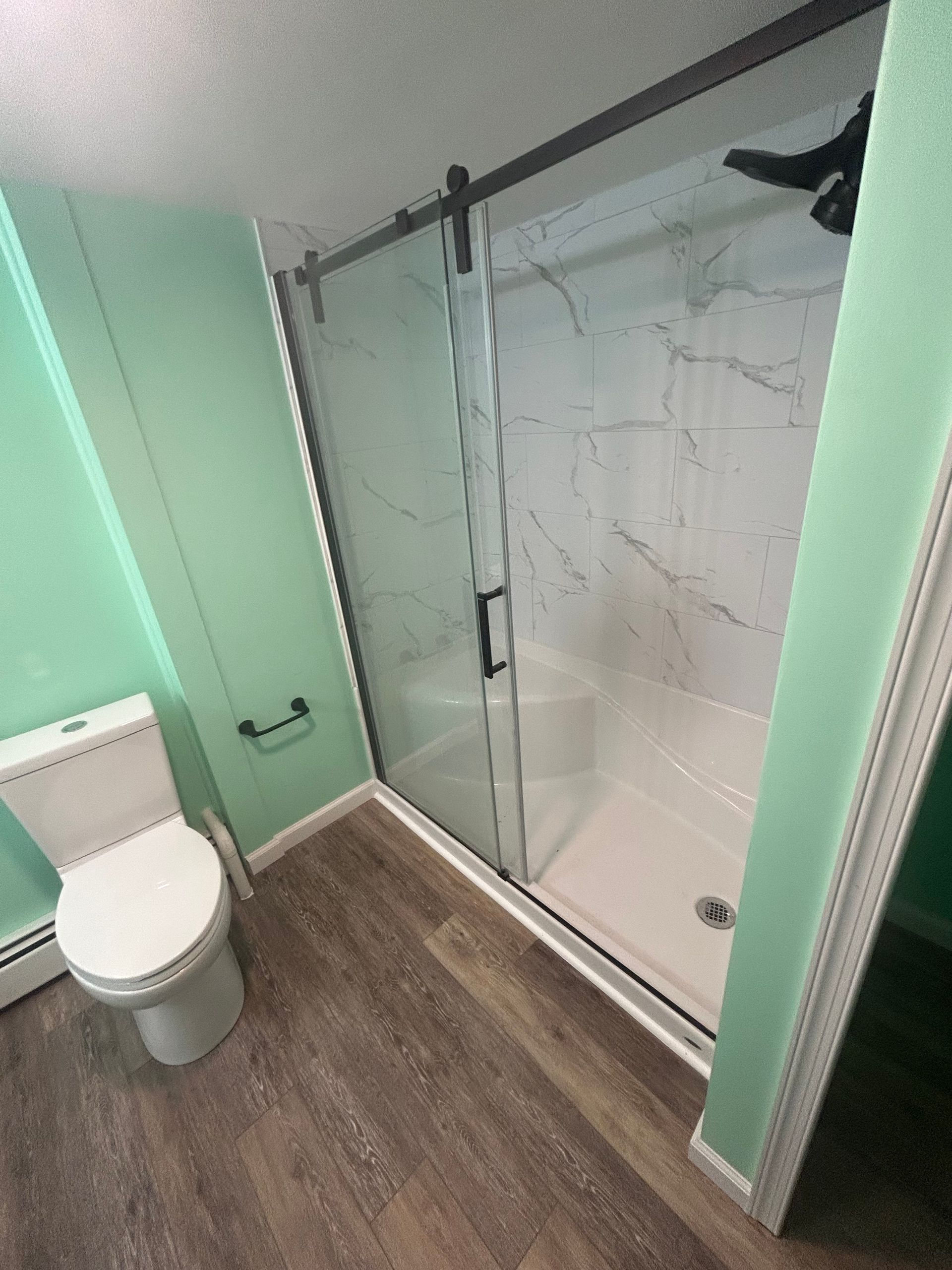 Bathroom with mint walls, a toilet, shower with glass door, and wood-look flooring.