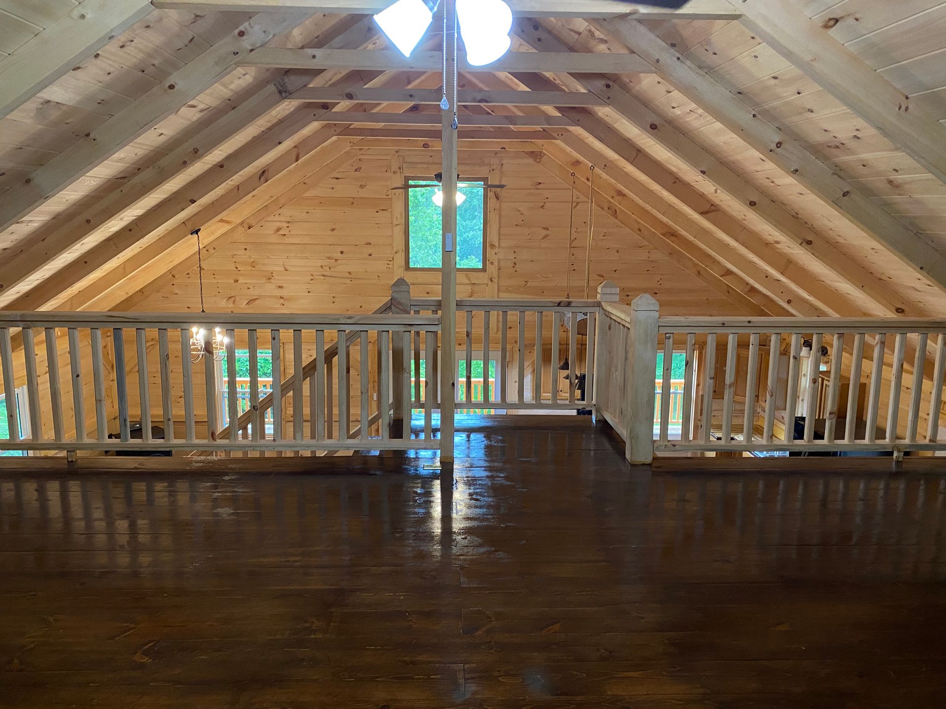 Interior of a wooden cabin loft with a railing, window, and exposed beams.