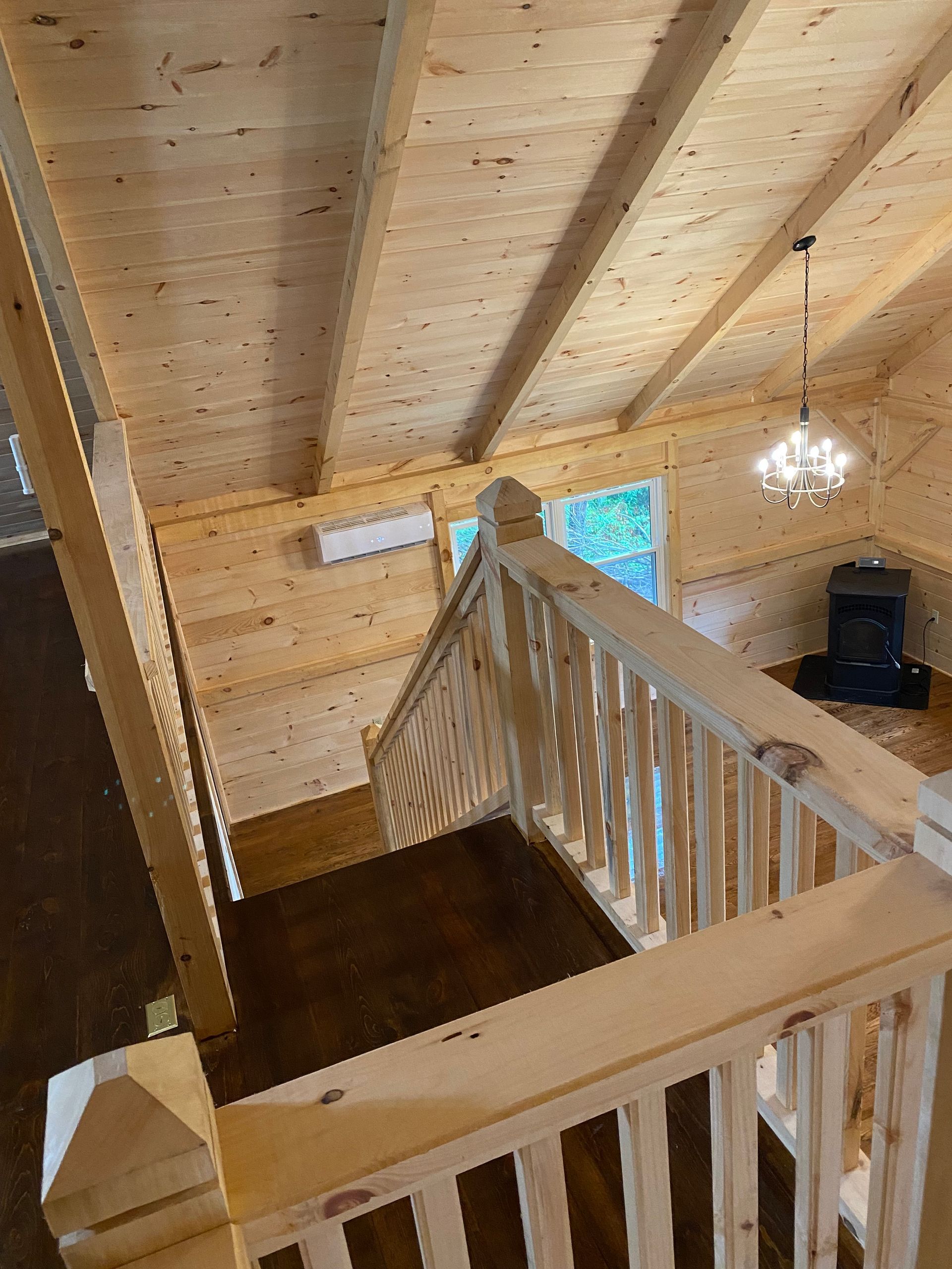Interior view of wooden cabin with staircase leading down, with fireplace, chandelier, and AC unit visible.