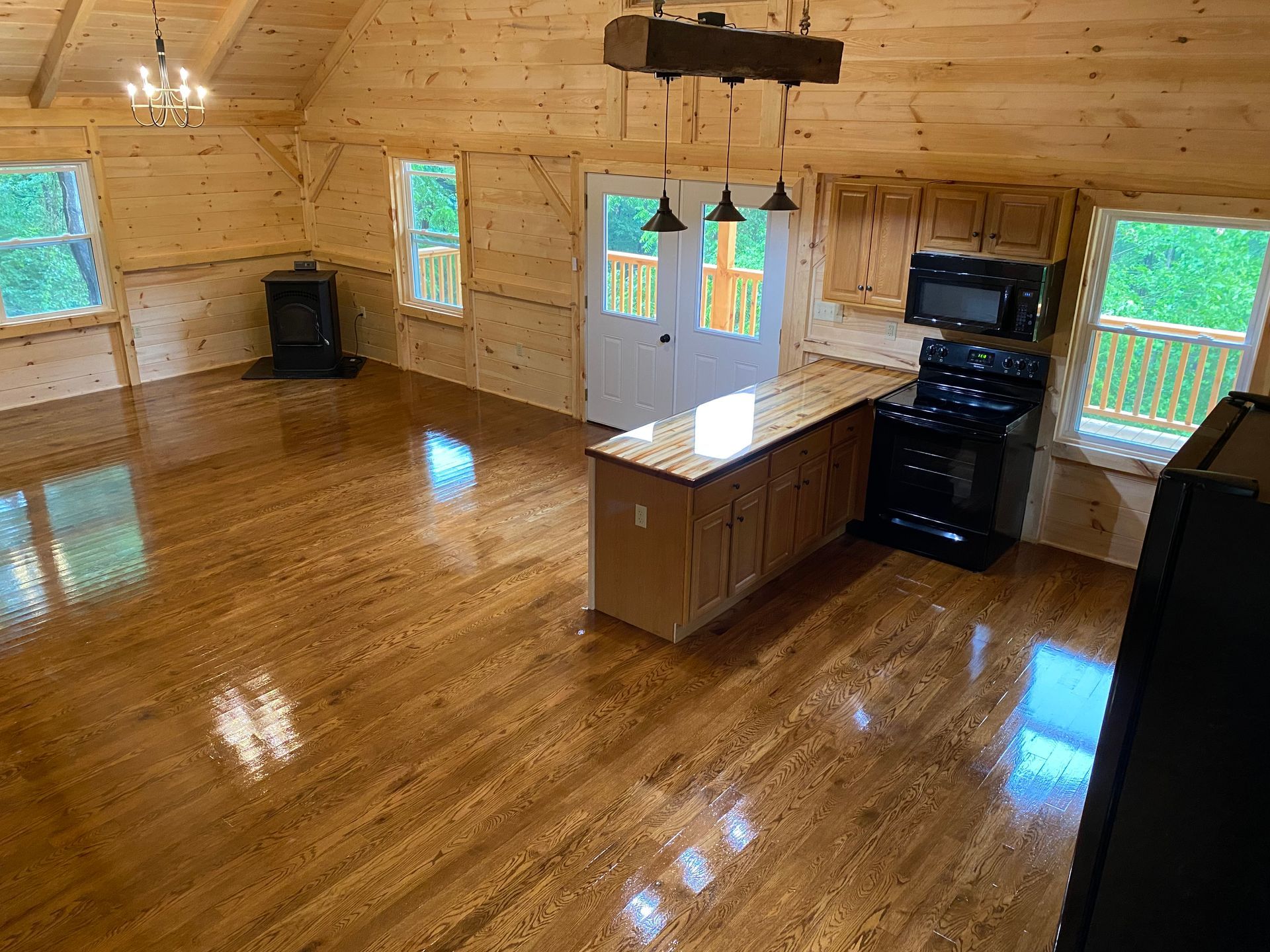 Interior view of a cabin with wood floors, kitchen, and living area, including a stove, island, and windows.